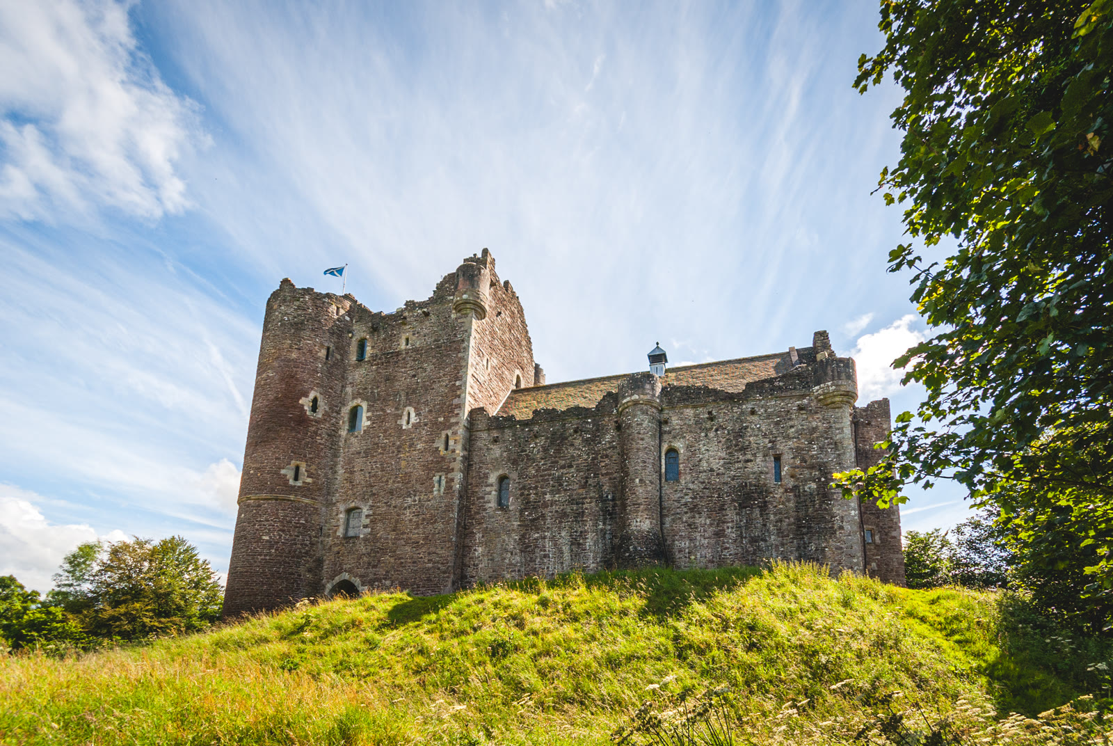 Doune Castle on its grassy mound under a blue summer sky, the tall gatehouse tower on the left and the hall range and curtain wall to the right, Stirlingshire.