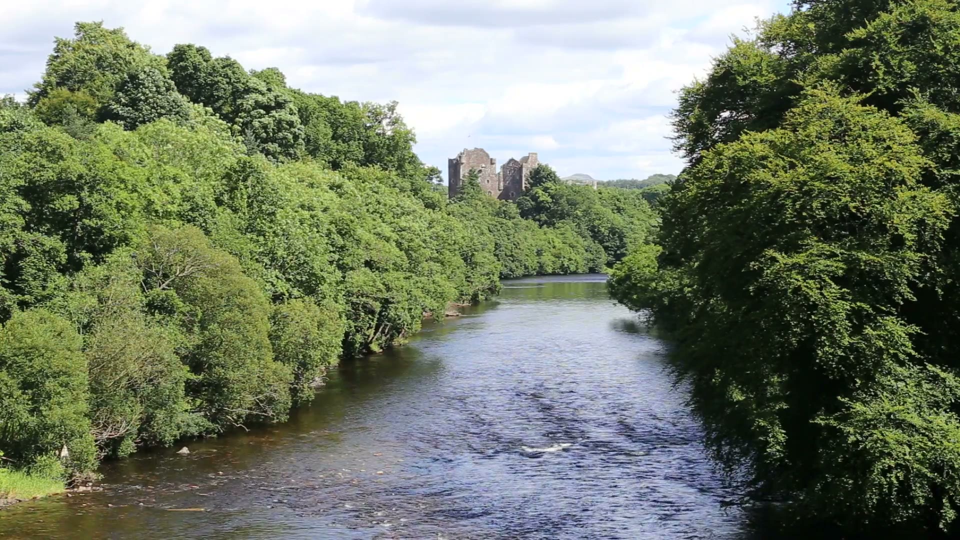 The River Teith flowing between full green trees towards Doune Castle.
