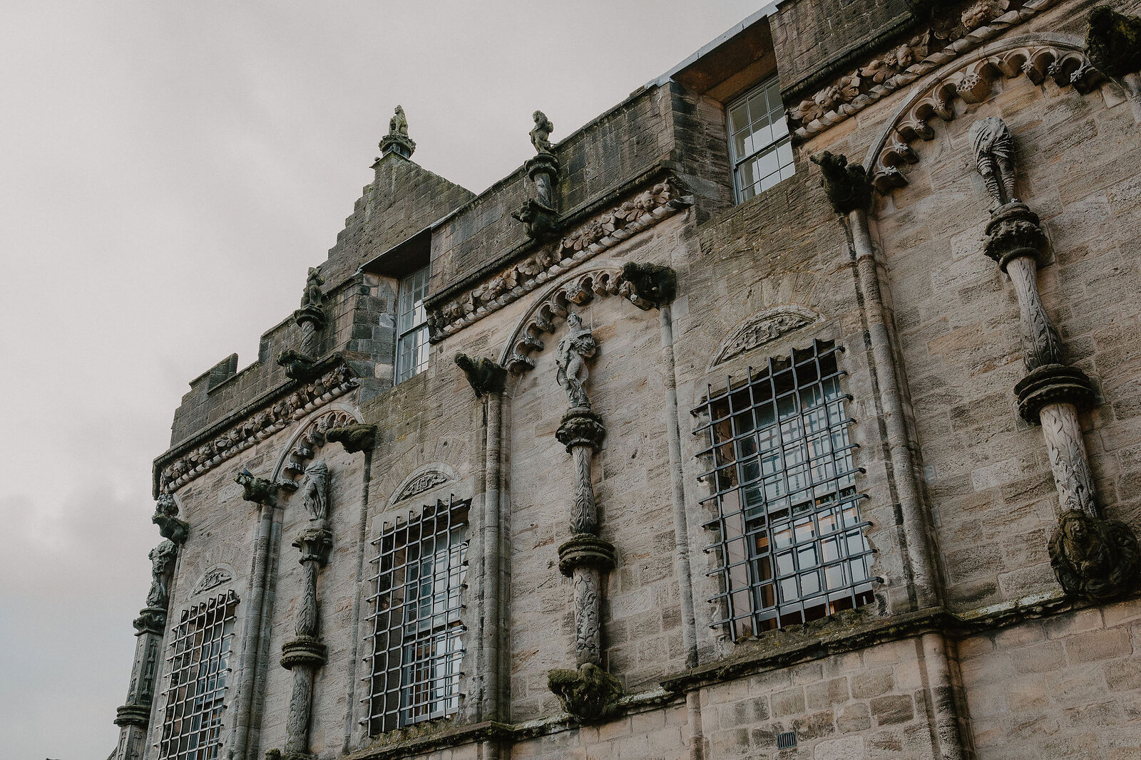 Carved stone statues stand between barred windows on the ornate facade of a royal palace, decorative pinnacles rising along the roofline.