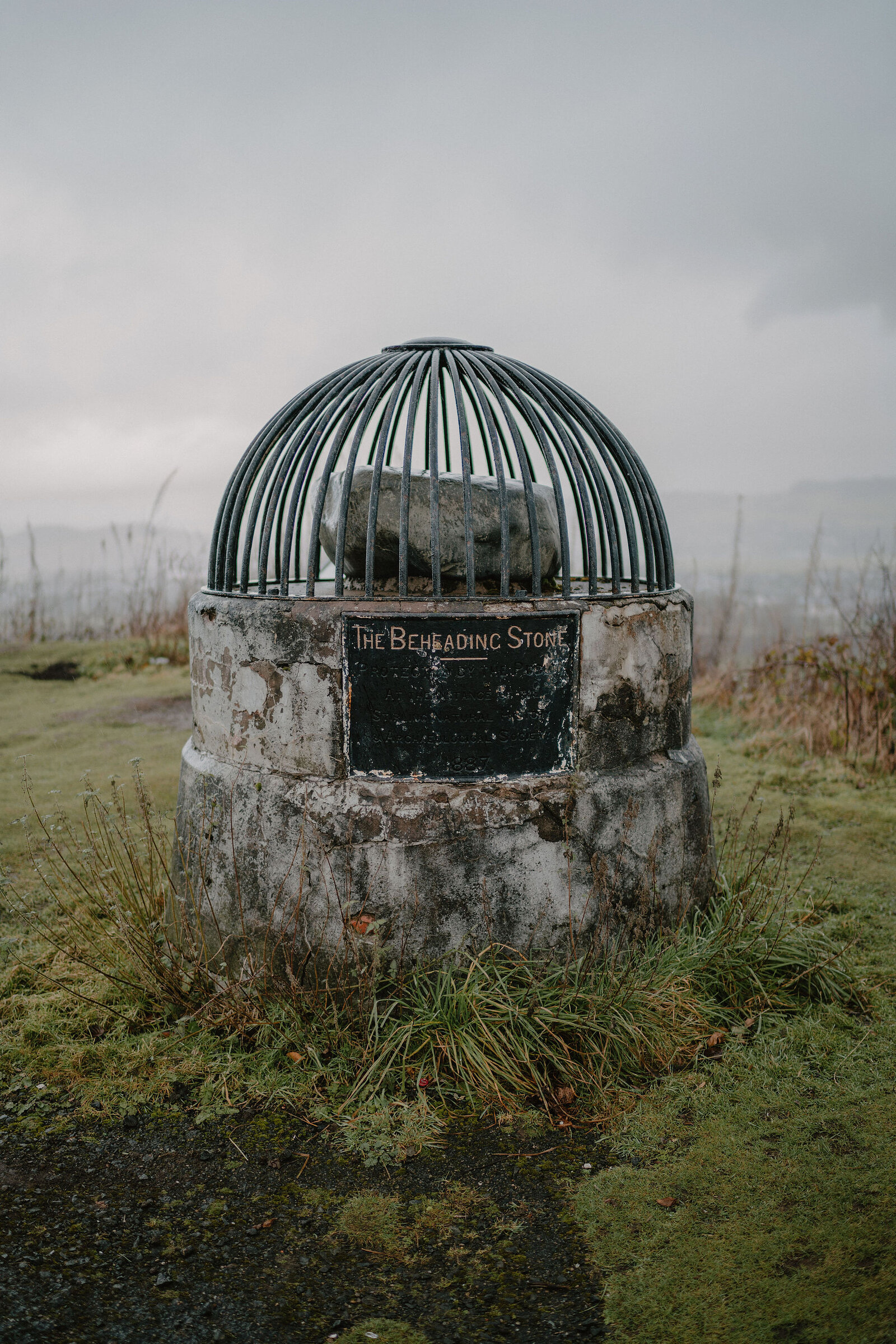 The Beheading Stone under its iron cage on a round stone plinth.