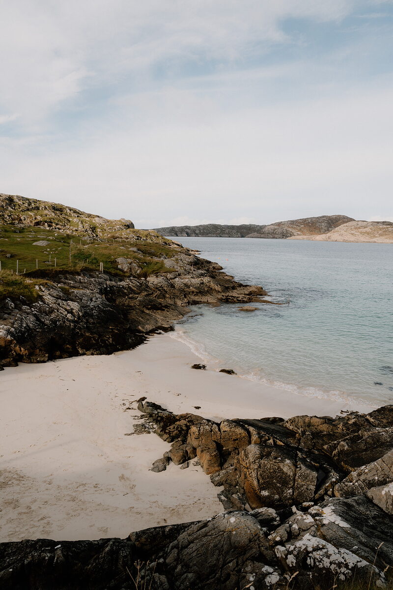 A sandy cove bordered by rocky headlands, calm turquoise water lapping the shore.