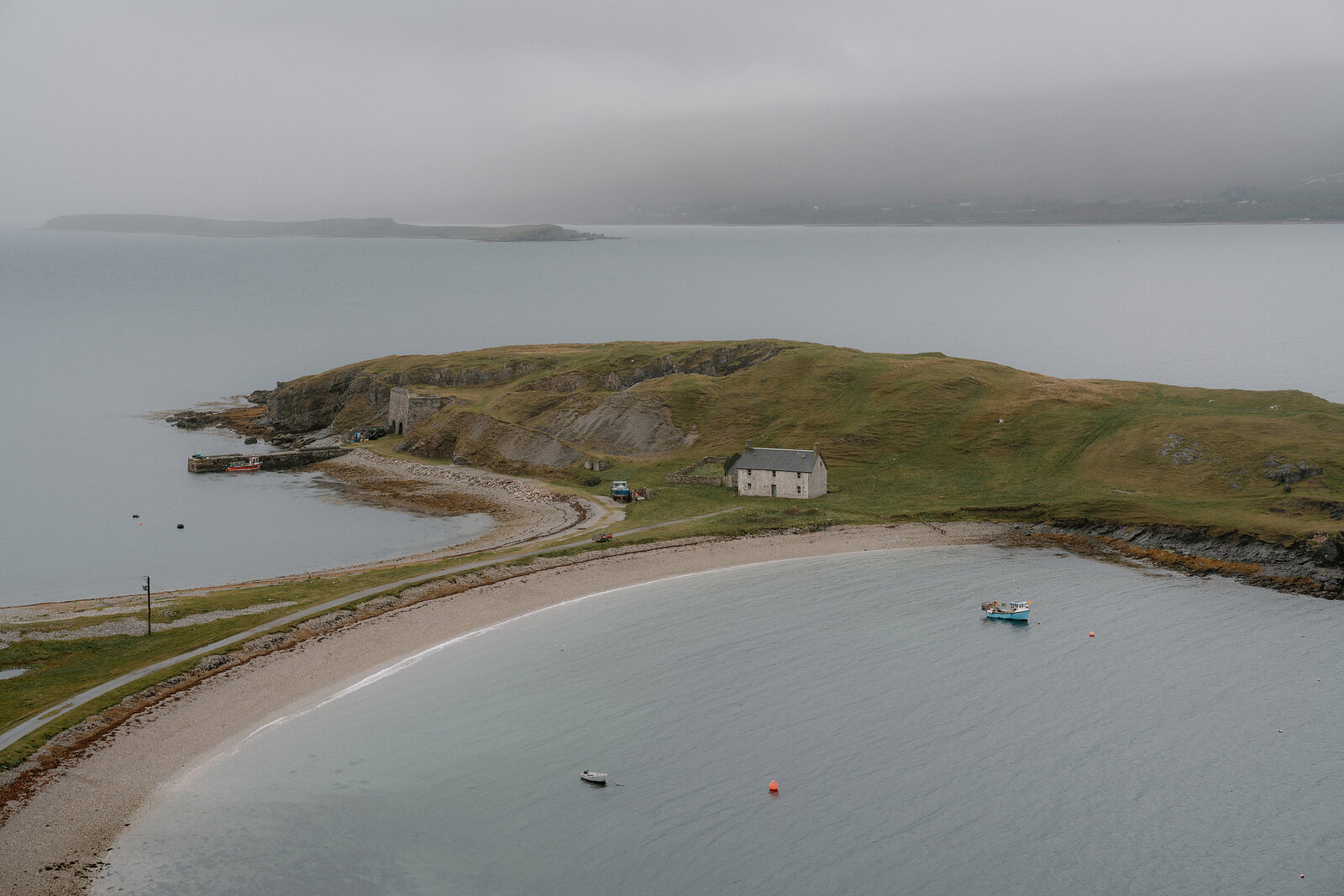 A curving sandy beach enclosed by a grassy headland, a small boat anchored near the shore