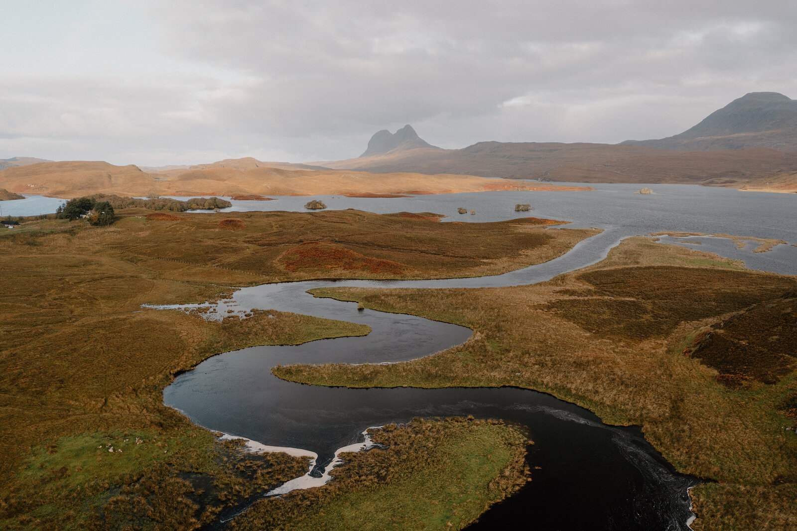 A winding river and loch below a distinctive peak, seen across open moorland