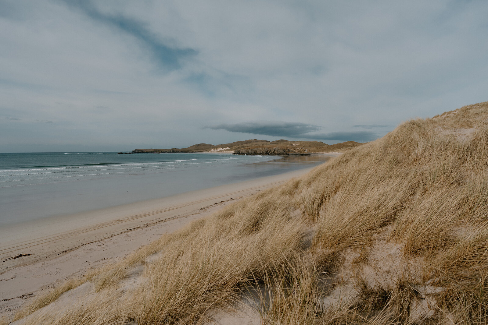 A sandy beach curving beneath dune grass, a rocky headland closing the bay