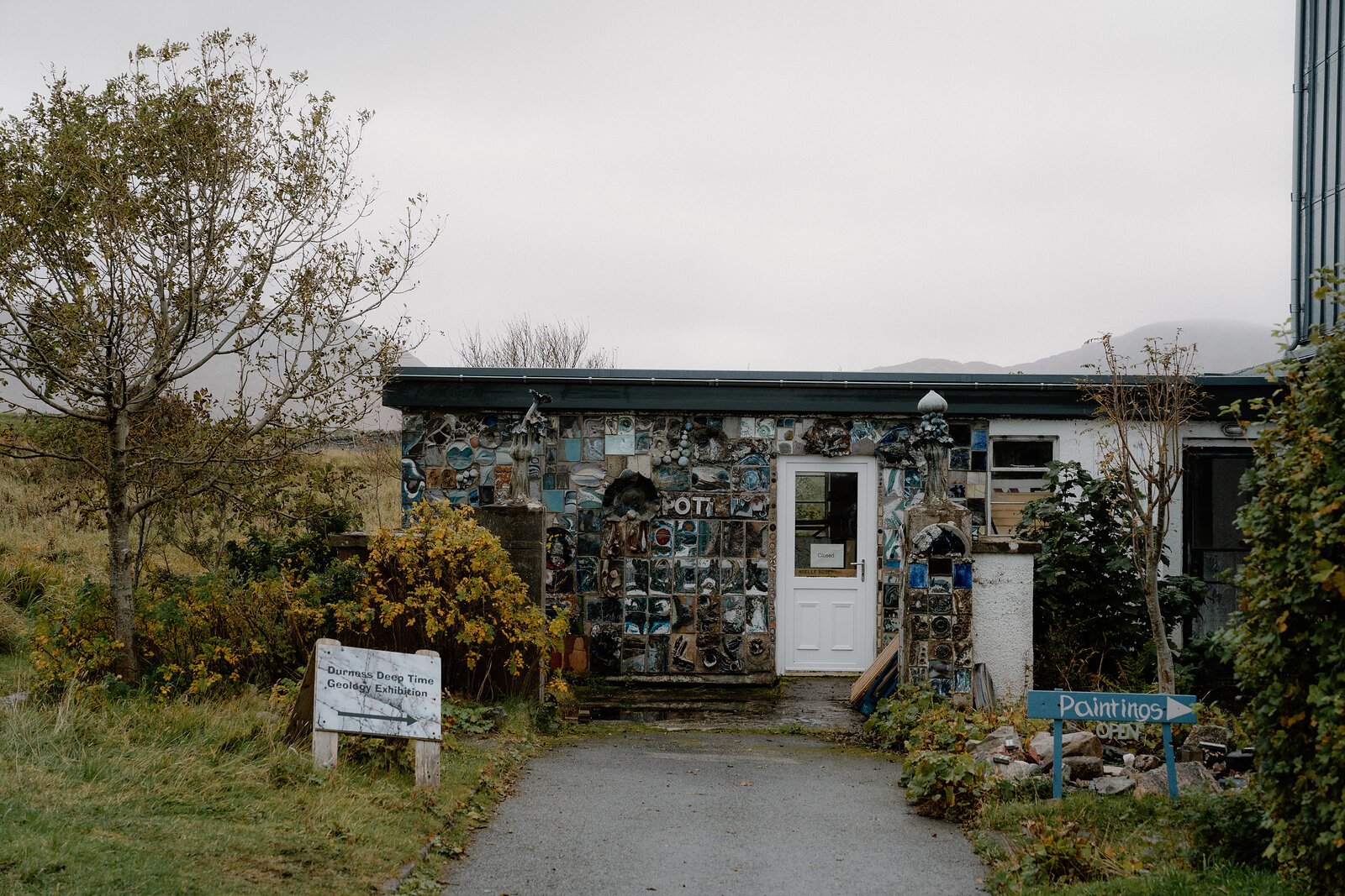 A mosaic-covered cottage with a sign reading Paintings, a path leading up to its door
