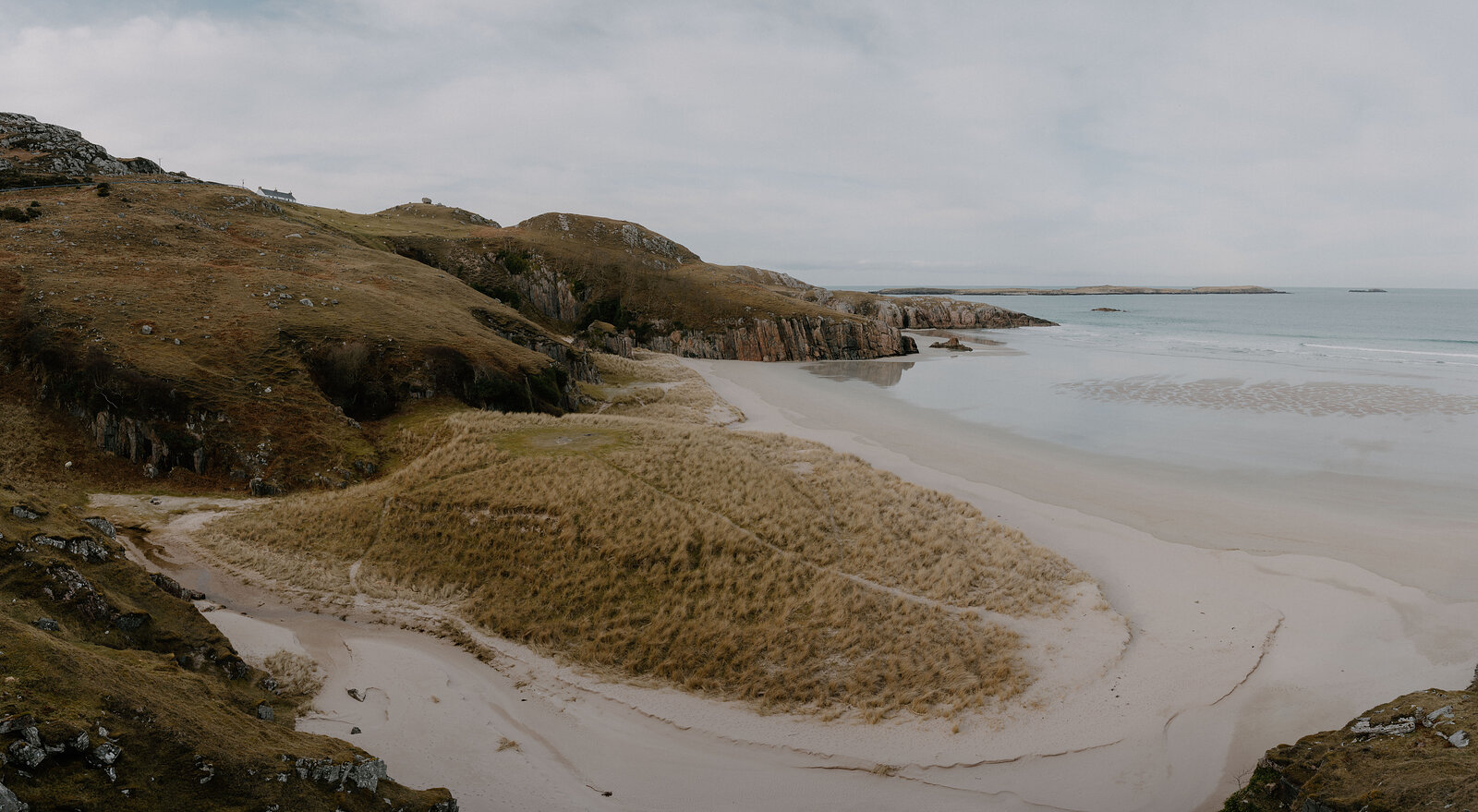 A curving sandy beach backed by dune grass and a rocky headland