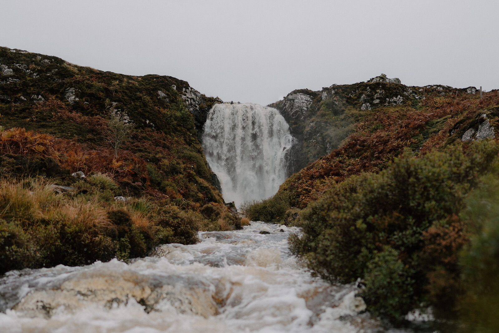A waterfall spilling through a mossy gorge into a fast-flowing burn, mist rising from the plunge pool