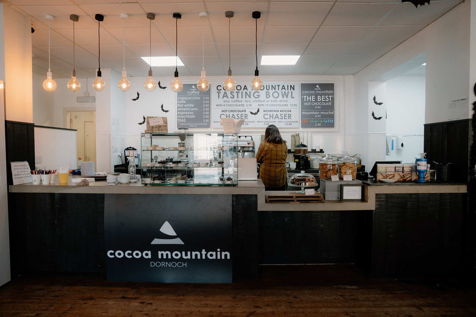 A customer orders at Cocoa Mountain's Dornoch counter beneath a chalkboard menu.
