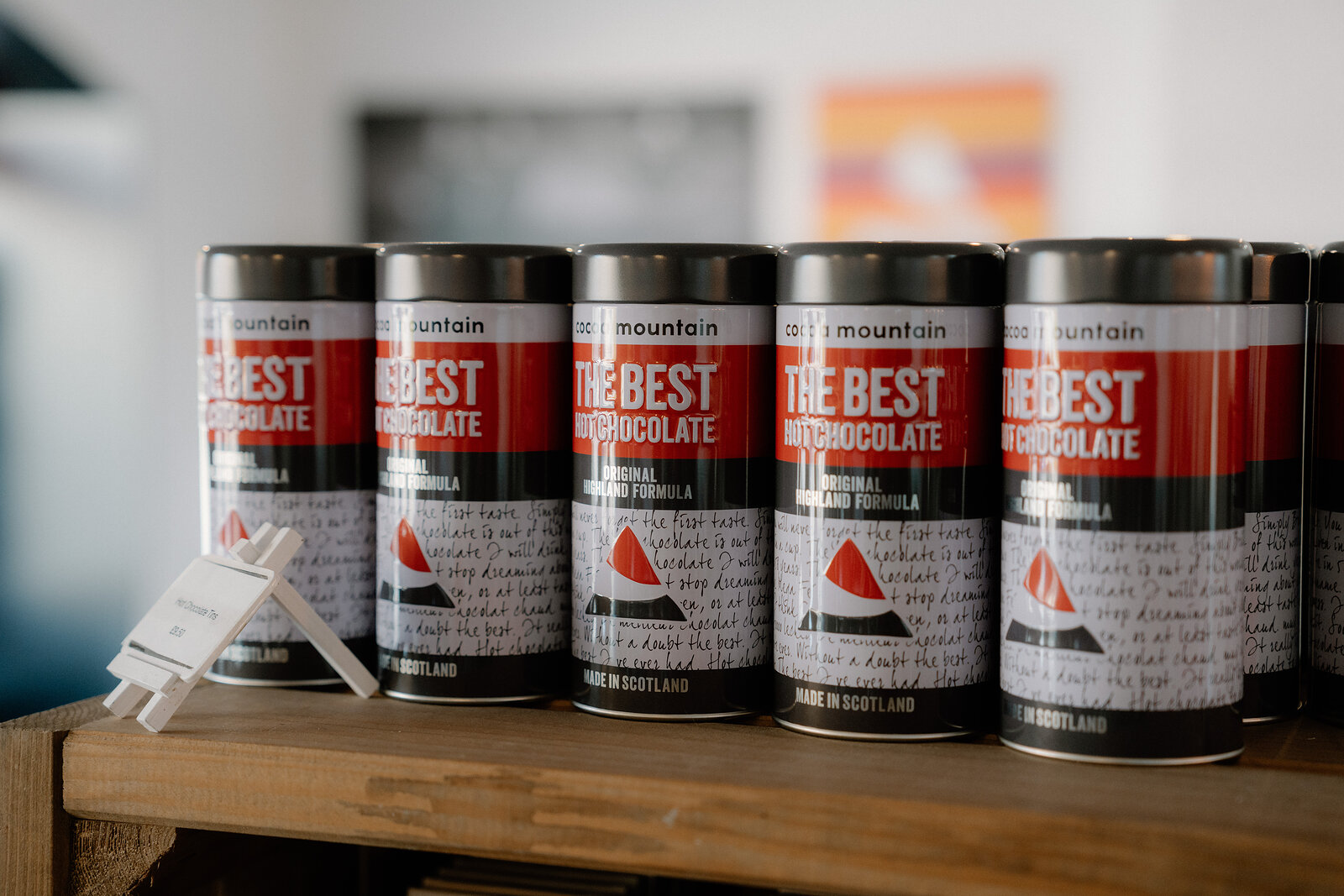 Tins of hot chocolate labelled 'The Best Hot Chocolate' line a wooden shelf.