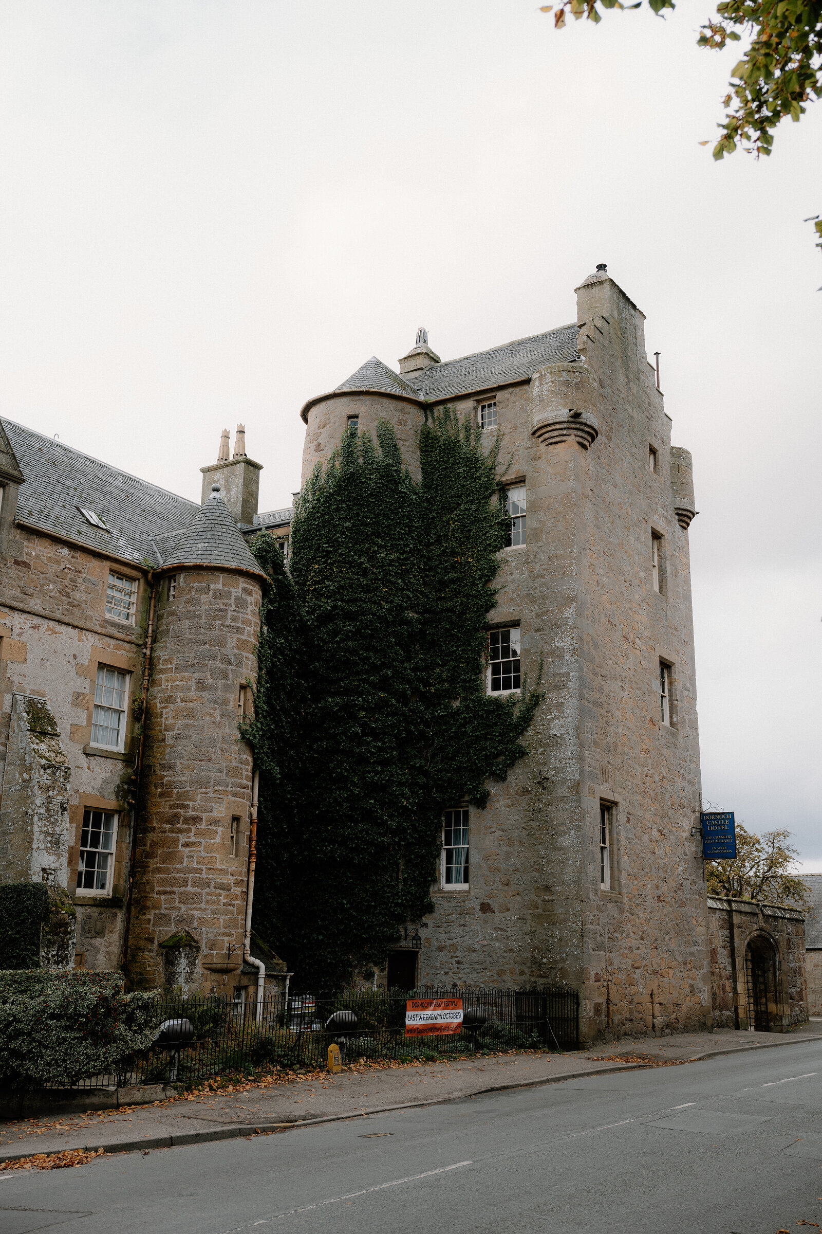 Ivy climbs a turreted stone tower beside a quiet street.