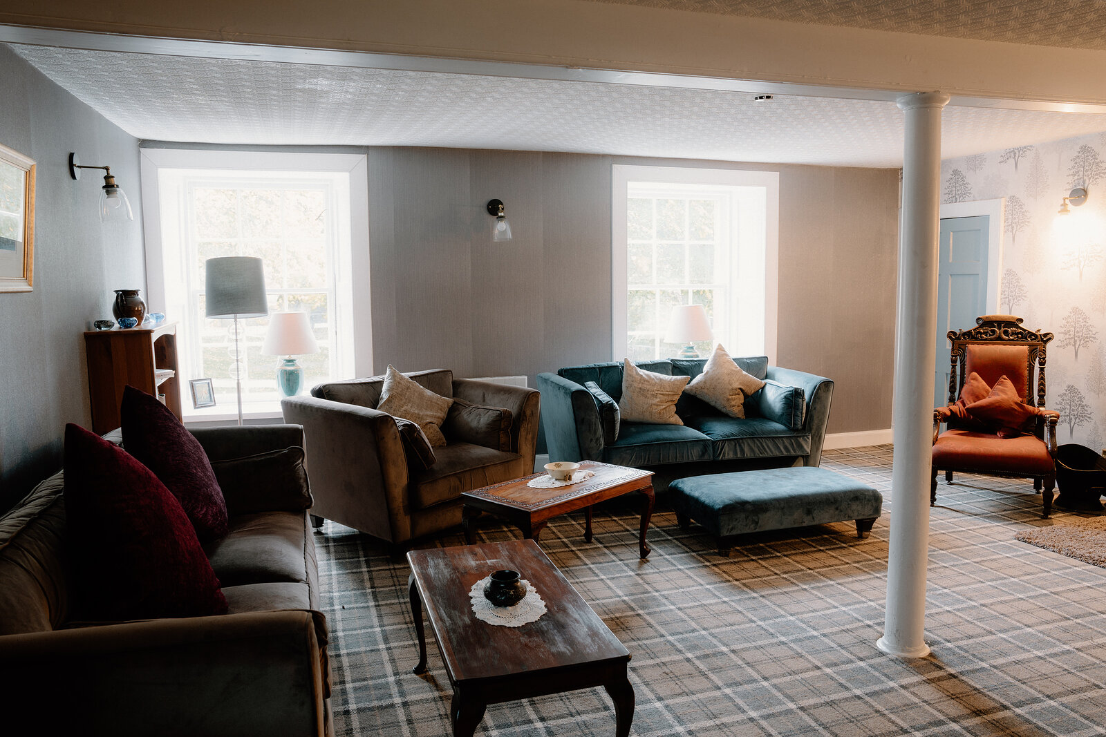 Teal and burgundy sofas surround a plaid rug beside an orange wingback chair.
