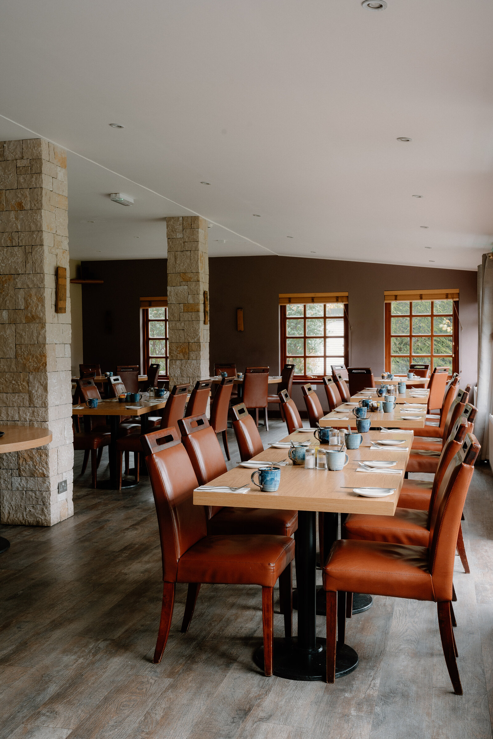 Orange leather chairs line dining tables set with mugs beneath stone pillars.