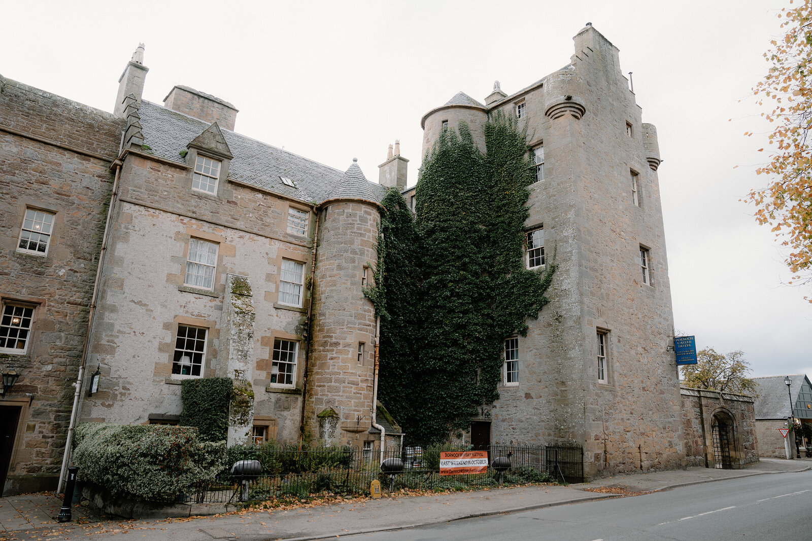 Ivy climbs a turreted stone building's central tower between conical roofs.