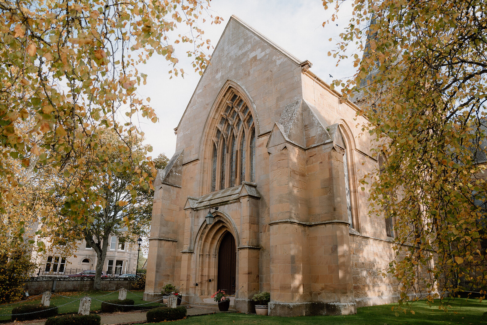 A Gothic sandstone church's arched doorway stands behind a row of gravestones.