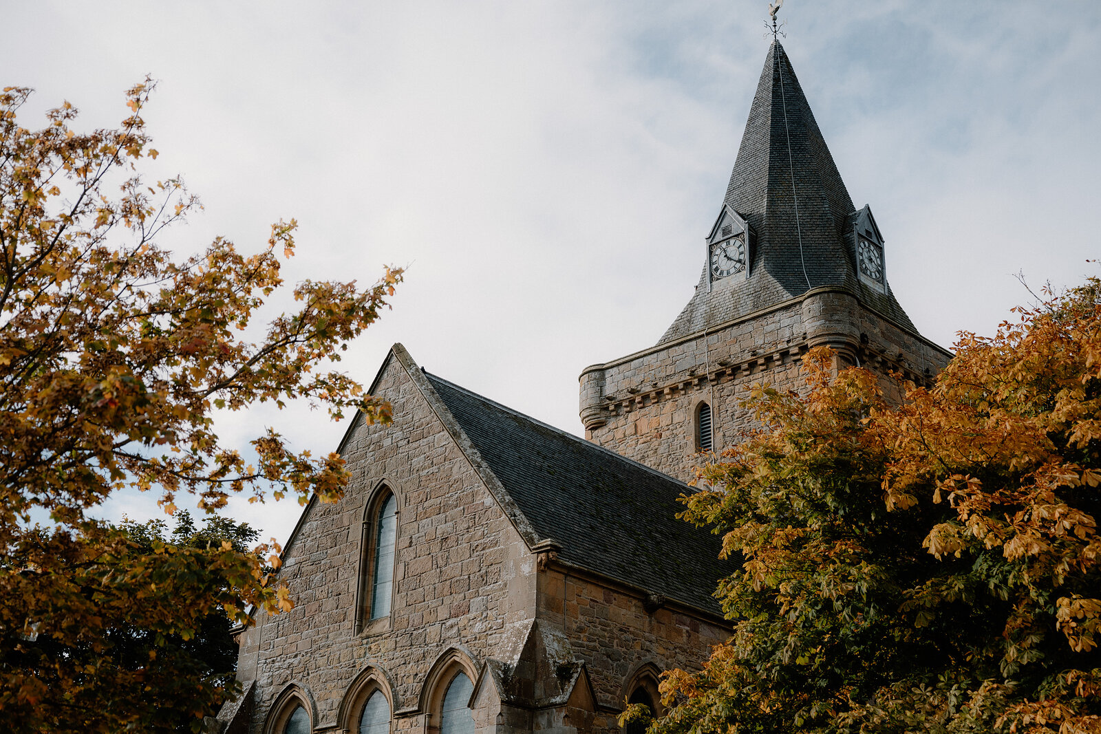 A church tower's spire and clock face rise above autumn-coloured trees.