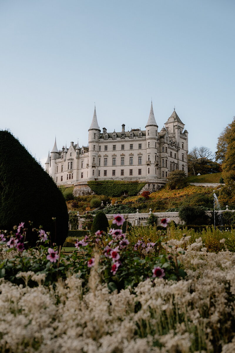 A turreted white castle rises above formal gardens dotted with autumn colour.