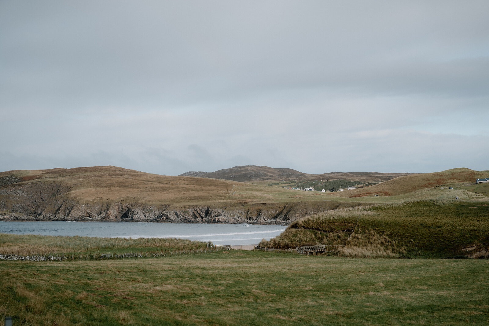 A curved bay of sand and sea framed by grassy headlands, houses scattered along the far shore