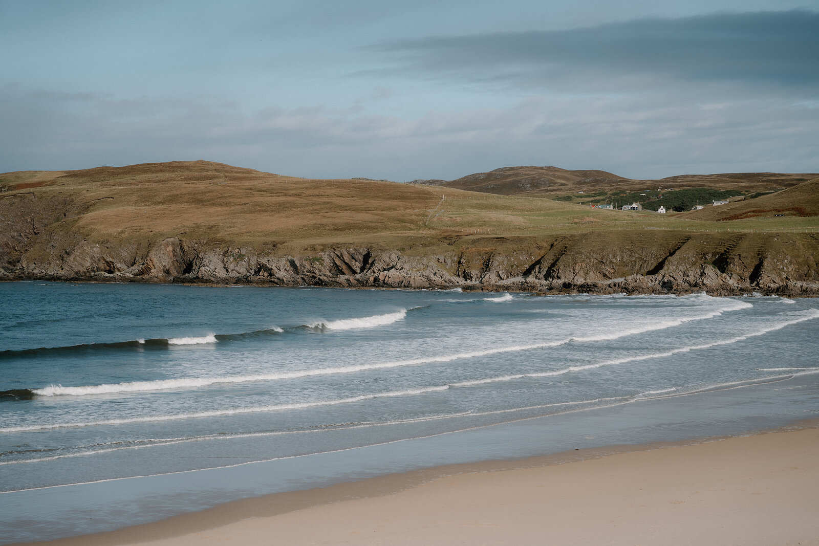 Waves rolling in along a wide sandy bay backed by grassy headlands