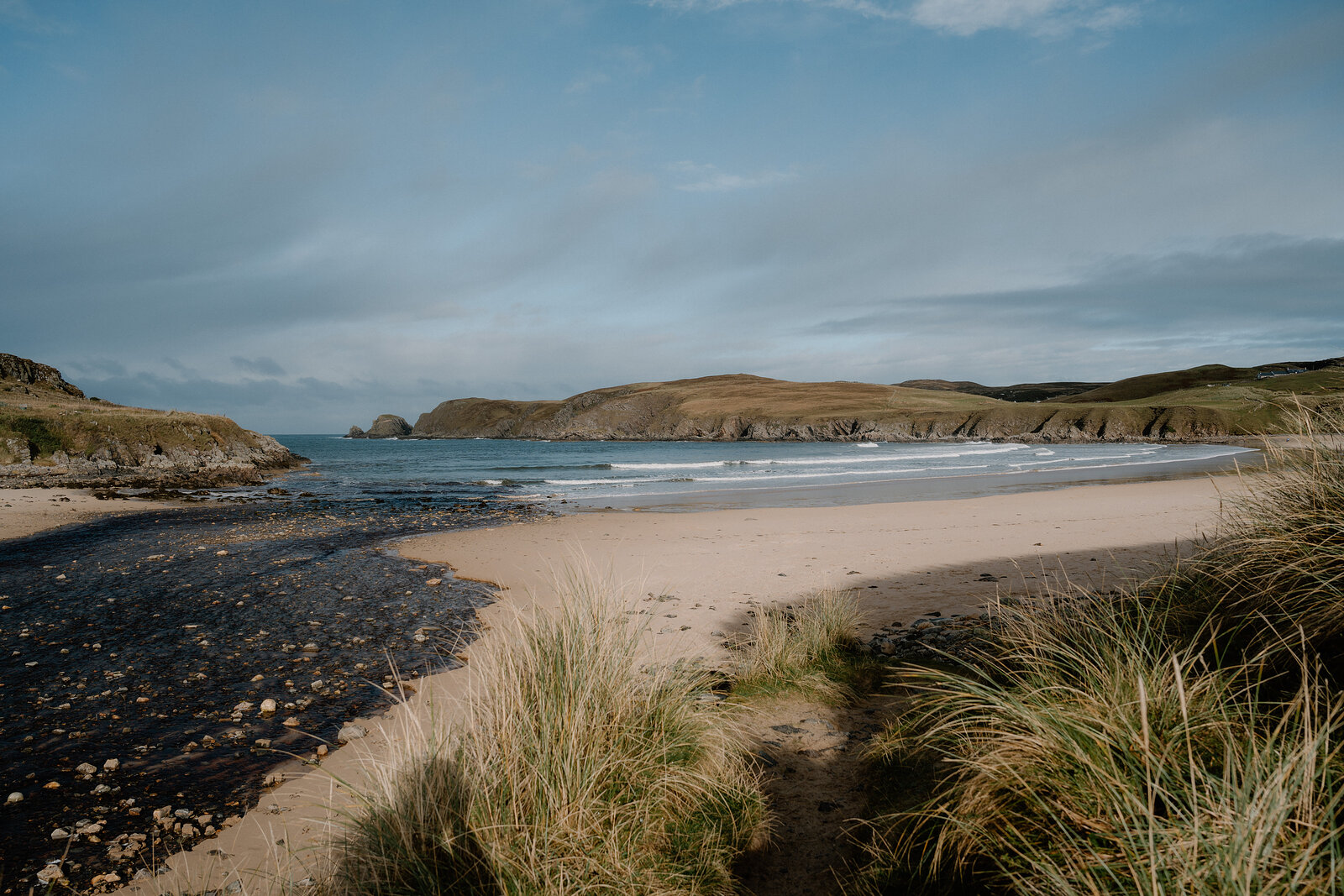 The burn running out across Farr Bay's pale sand to the sea, marram grass in front and the low cliffs of Ard Beag across the bay.