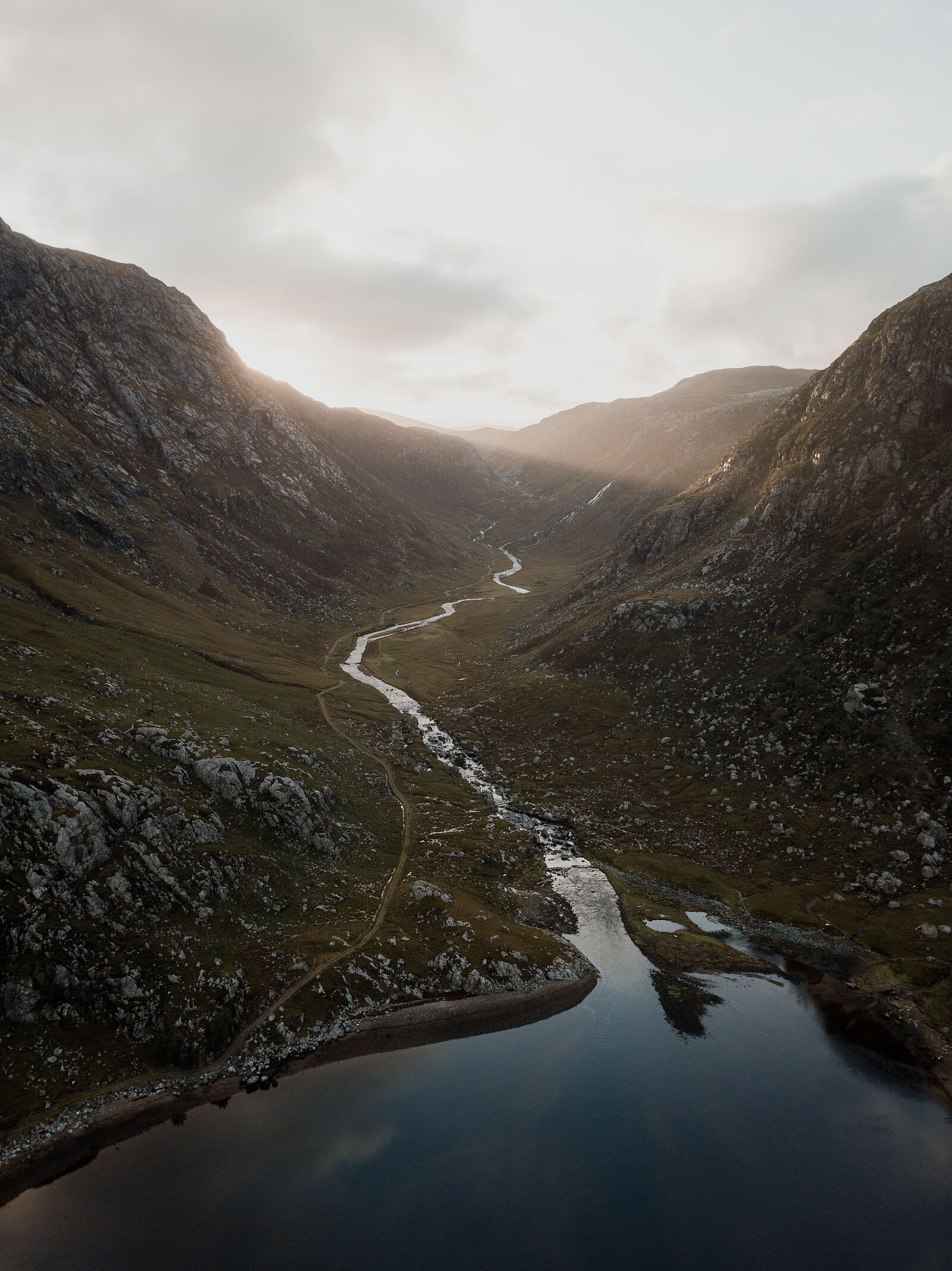 An aerial view of a steep-sided glen, a river winding down to meet a loch at dawn.