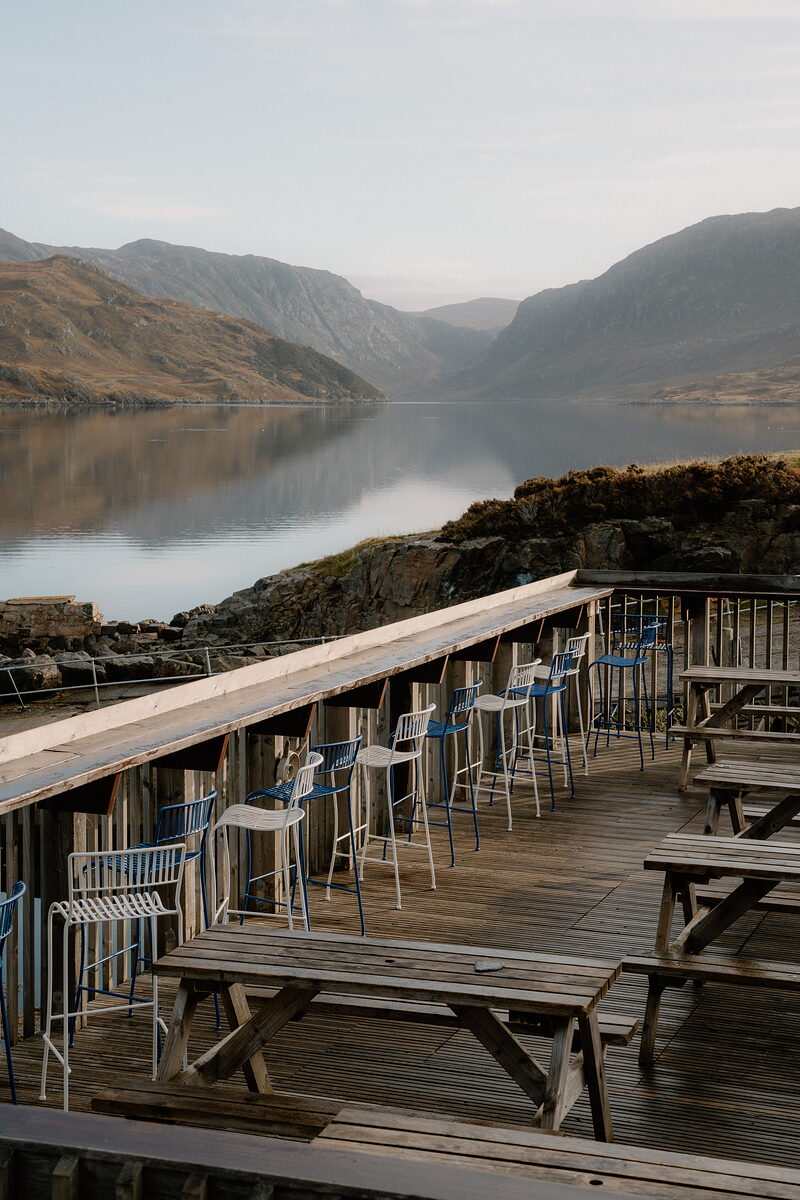 The Kylesku Hotel's timber deck with bar stools and picnic tables looking out over the loch and mountains.