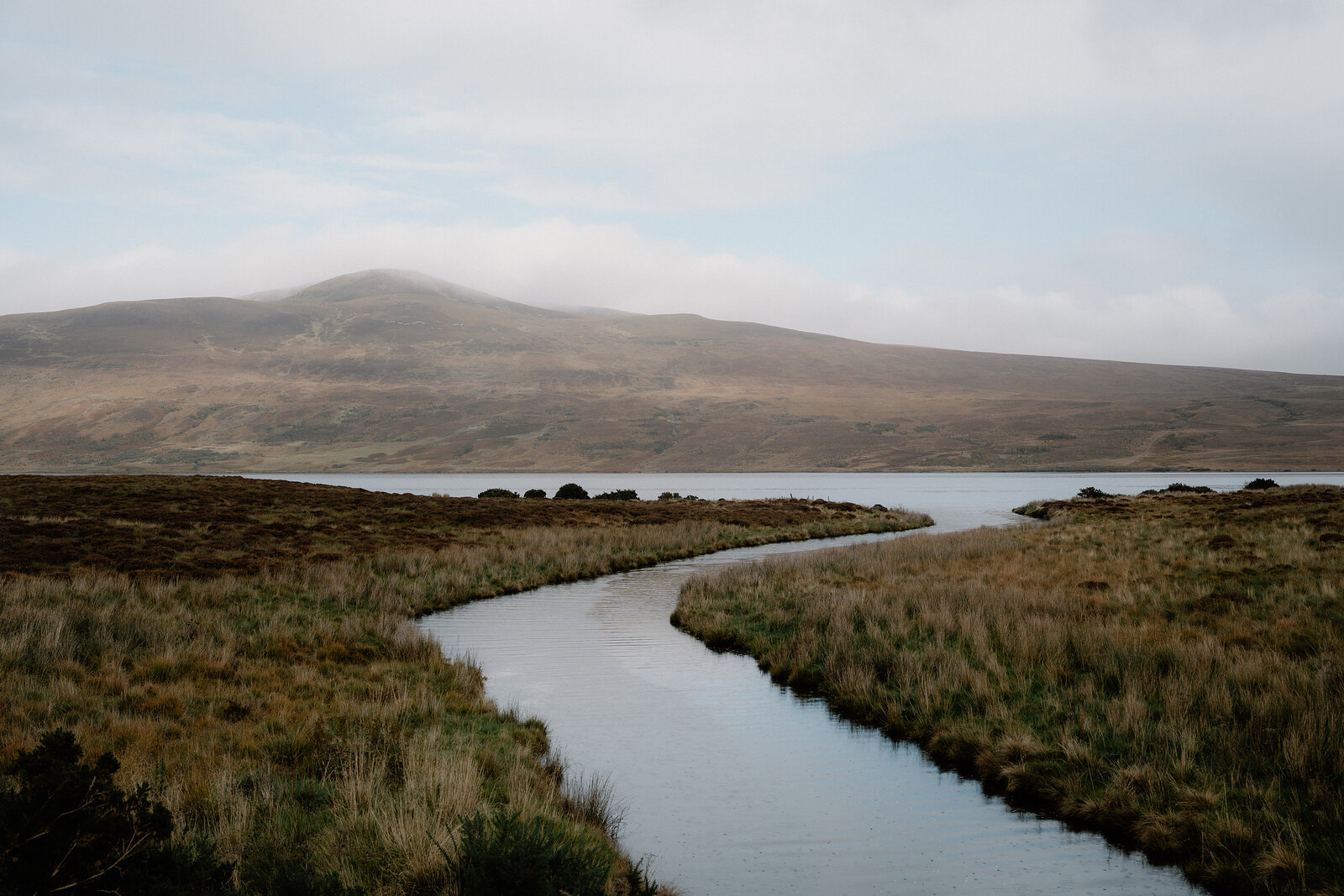 A stream winding through moorland beneath misty hills.