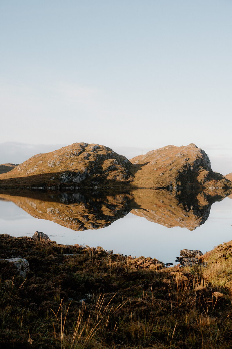 Sunlit hills reflected in a still loch at Loch na Thull.
