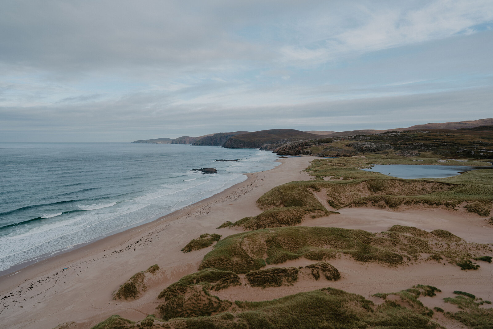 Pink-tinged sand curves along a bay backed by dunes and small lochs.