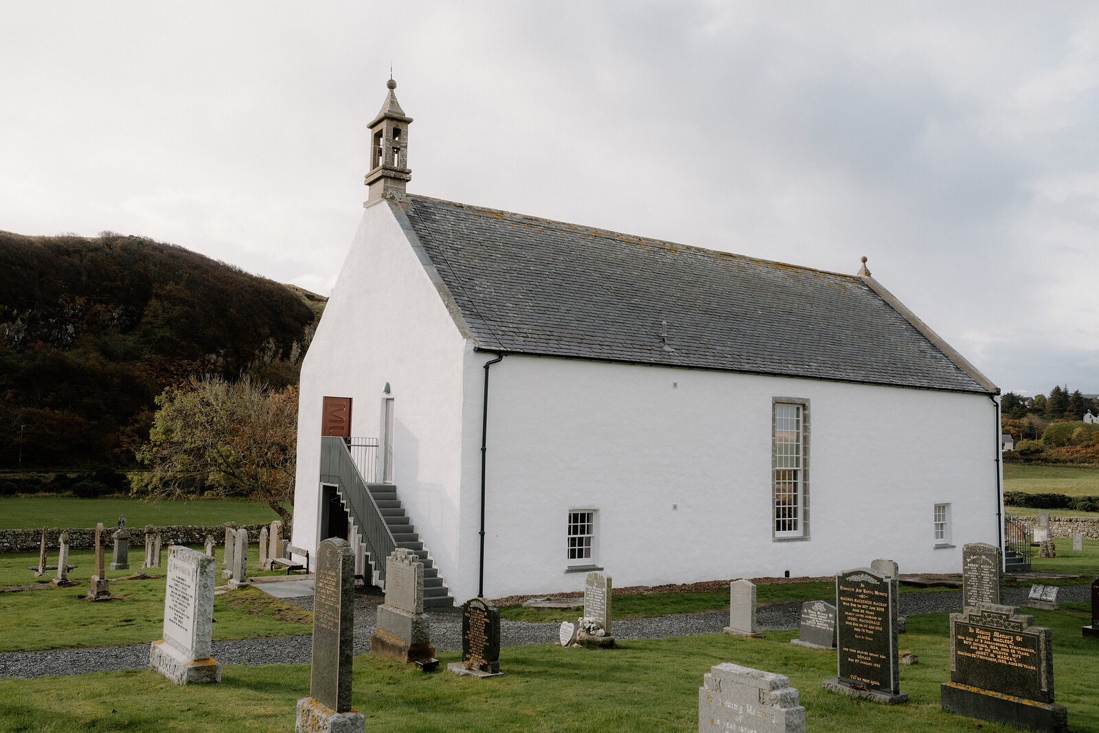 Strathnaver Museum's white former church stands within a walled graveyard on open grassland.