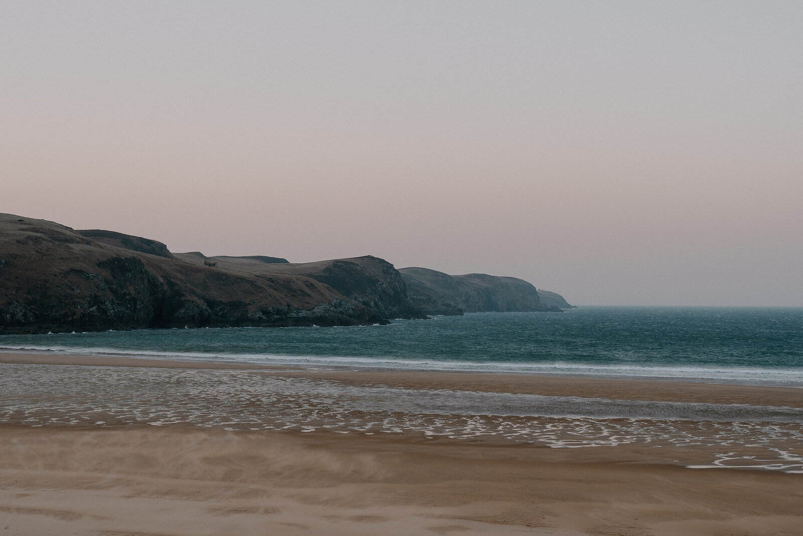 Dusk light falls over cliffs bordering a sandy beach.