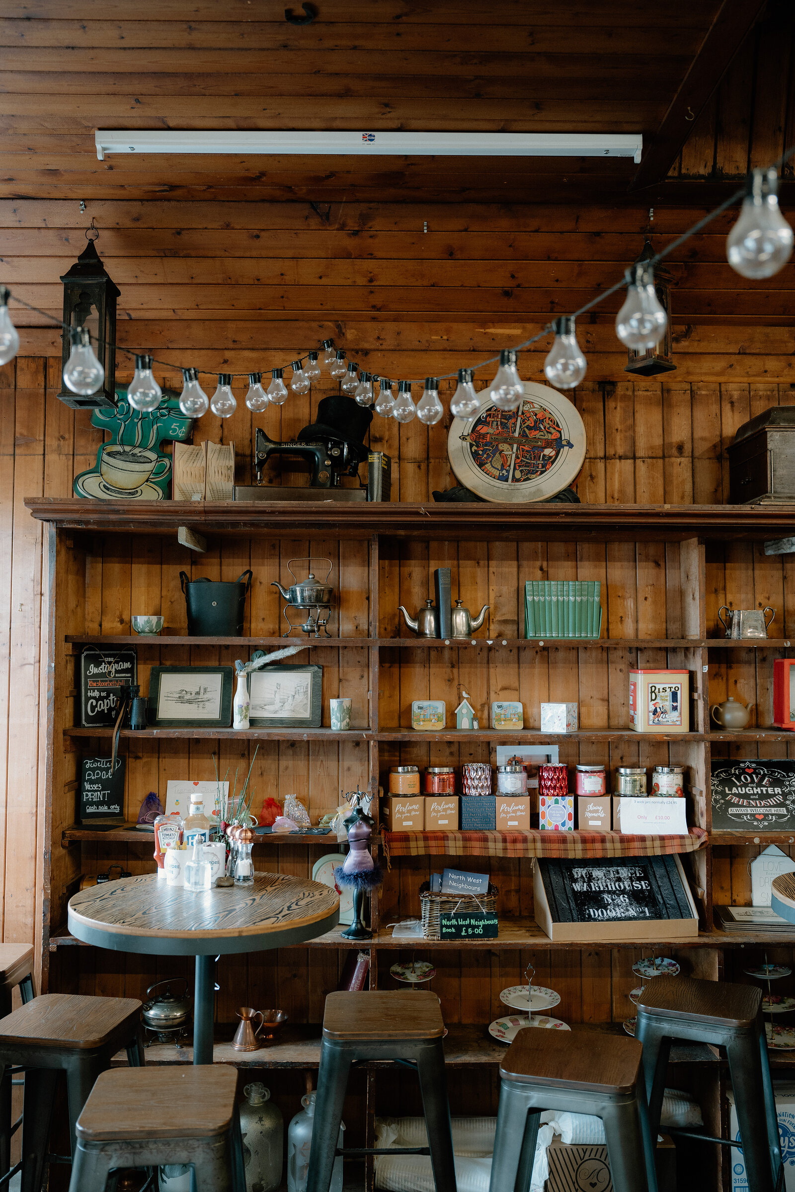 Vintage bric-a-brac lines wooden shelves above stools in a rustic café.