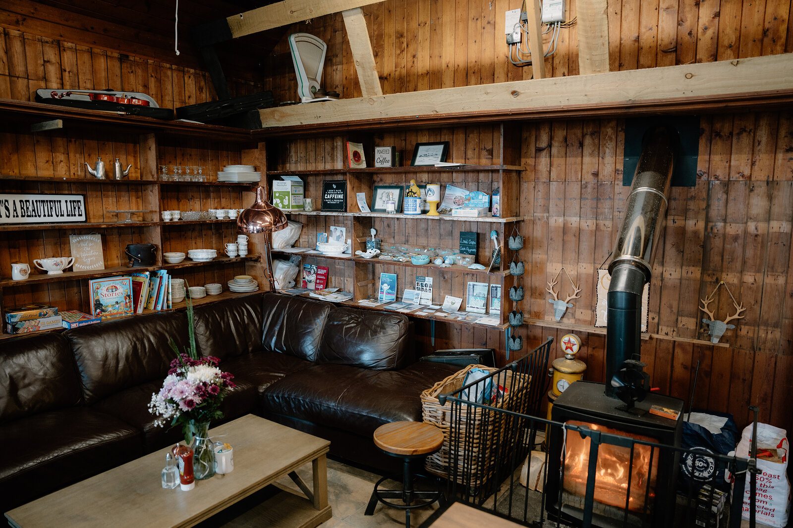 A leather sofa faces a wood burner in a timber-panelled room lined with shelved books and antlers.