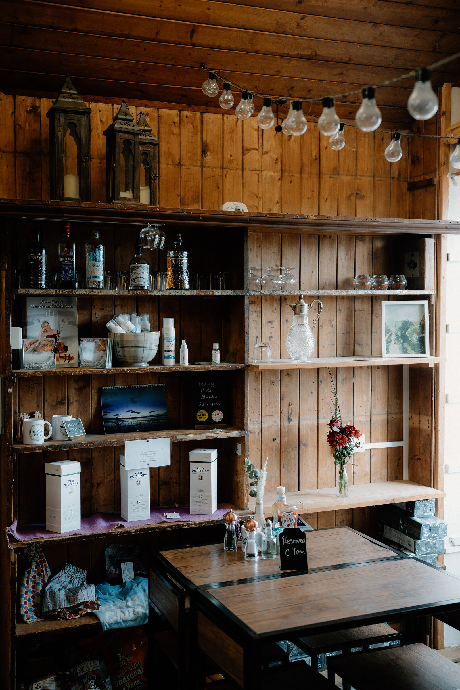 Gin bottles and gift jars line wooden shelves strung with hanging bulbs.