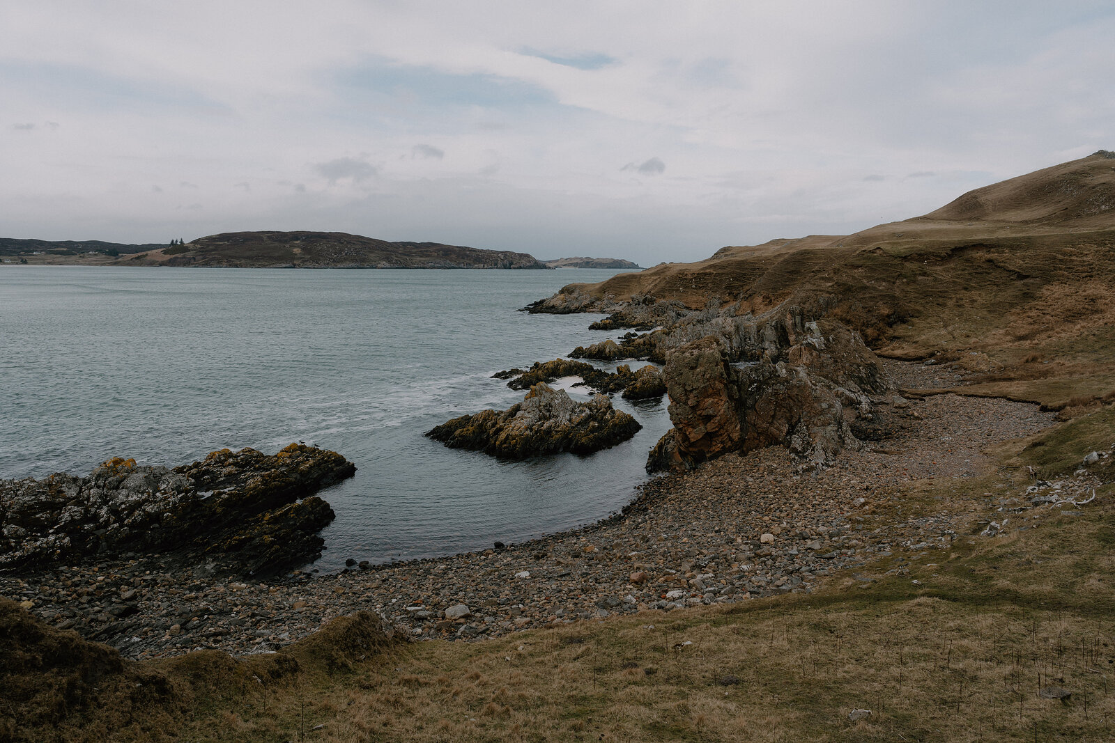 Rocky outcrops frame a quiet coastal cove, with hills rising beyond the water.