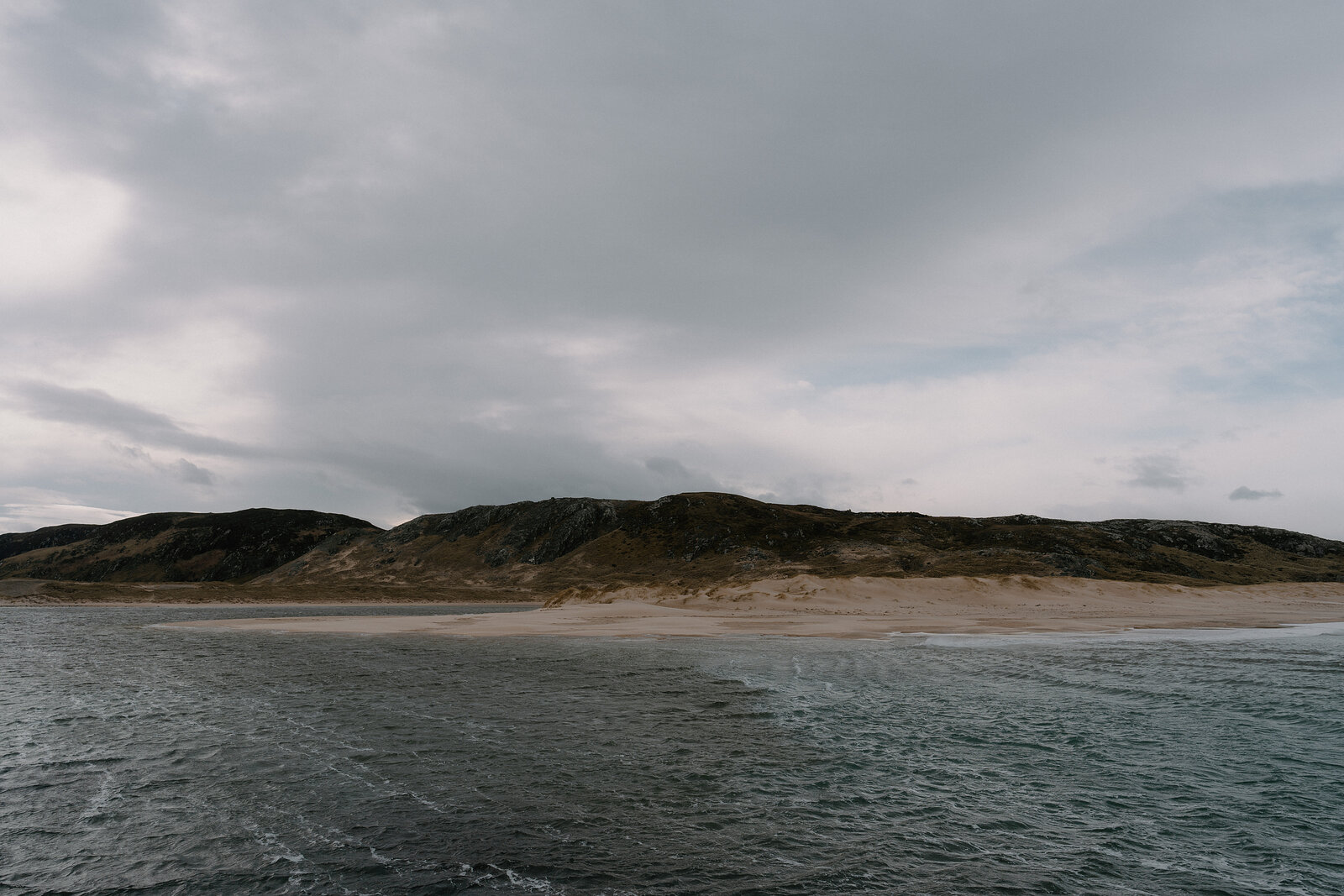 A sandy beach curves beneath a dune-covered headland.