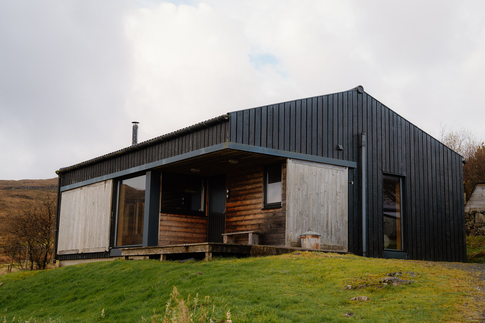 The Black Shed on Skye: a low building in black corrugated metal and pale larch, its porch open to the grass and hills