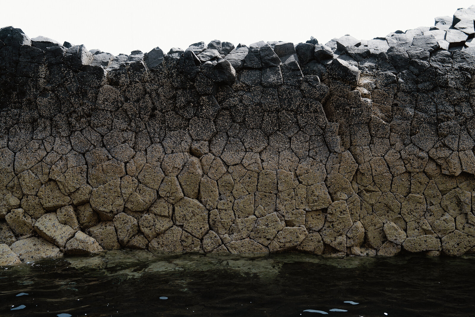 The hexagonal tops of basalt columns form a honeycomb pattern where the rock meets the water's edge.