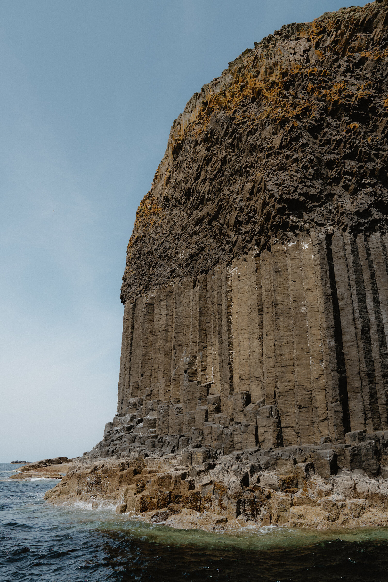 Tall hexagonal basalt columns form a sheer cliff face rising from the sea, waves breaking at the rocky base.