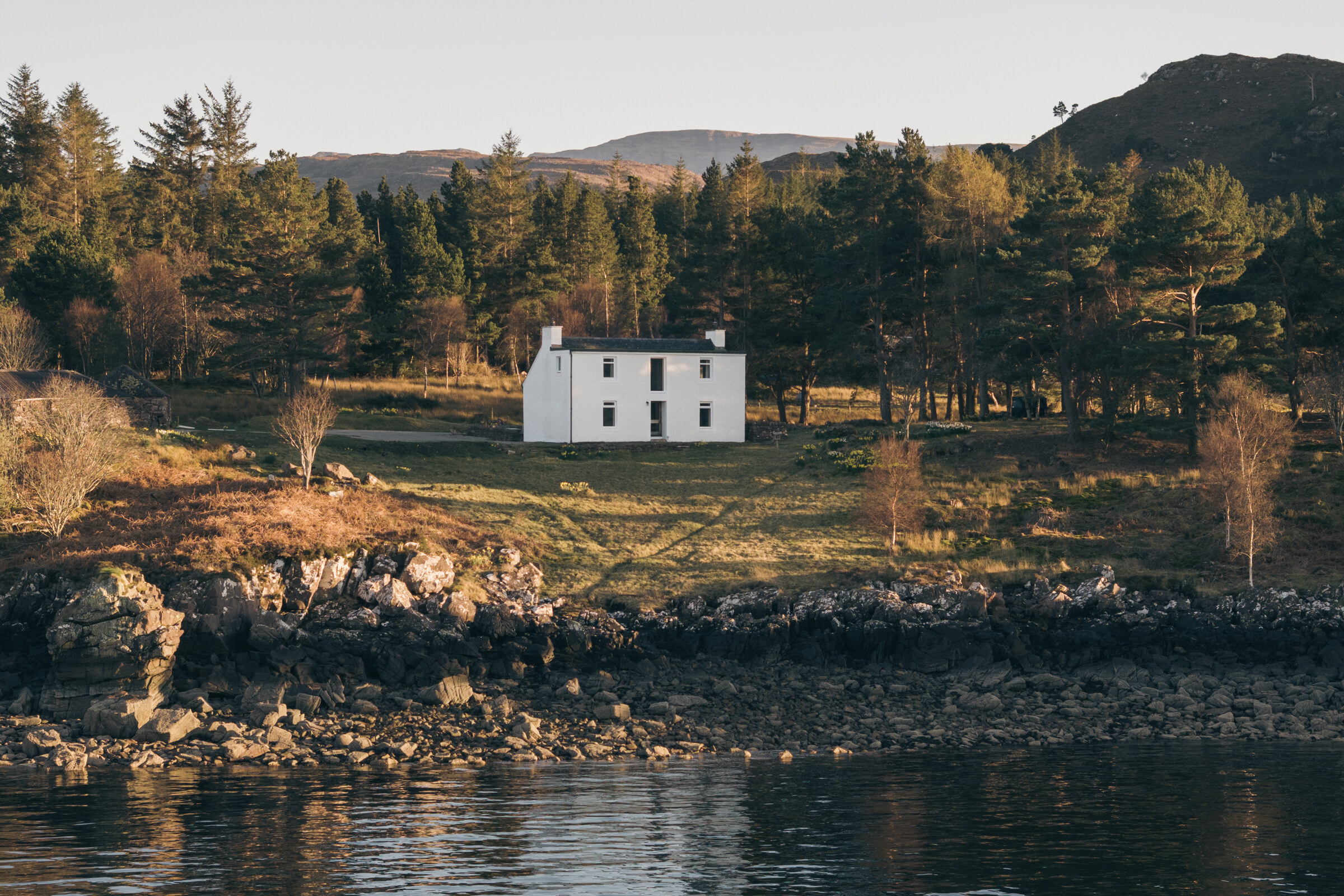 Rhuroin, a white two-storey house, among Scots pines above the rocky shore of Loch Shieldaig.