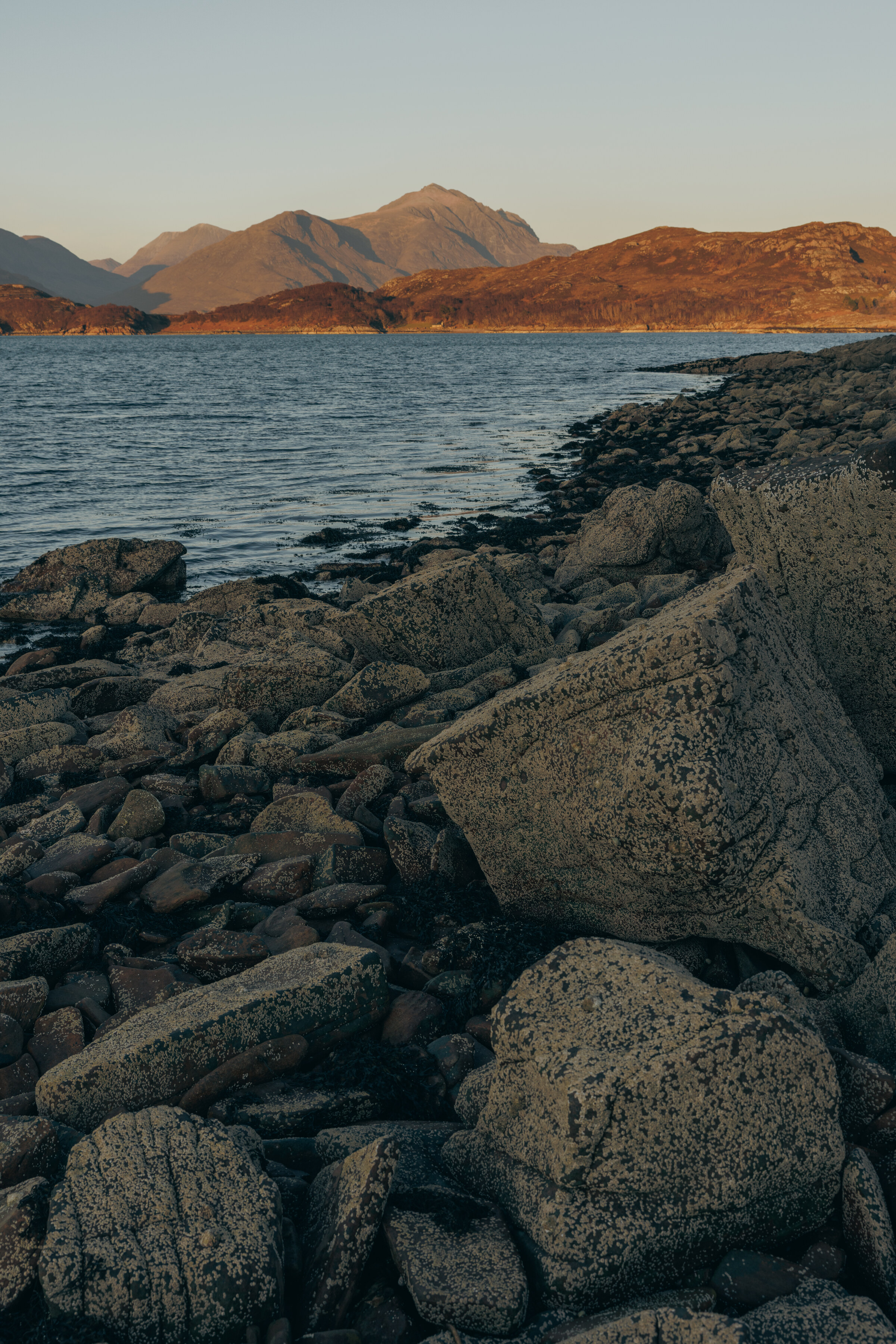 The rocky shore of Loch Shieldaig, with the hills across the water in evening light.