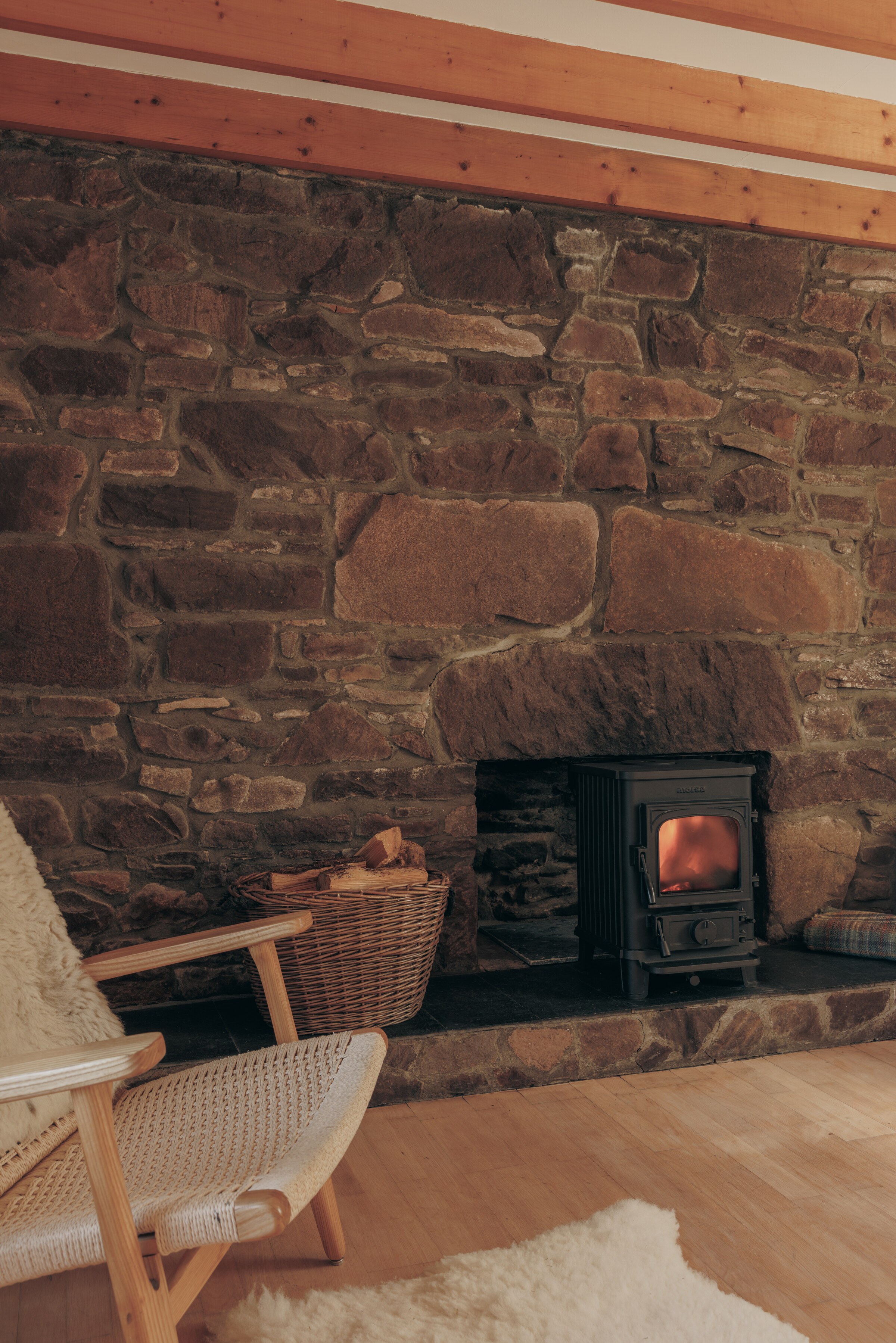 A wood-burning stove set into a wall of bare stone in Rhuroin’s sitting room, with a wooden chair and a sheepskin.