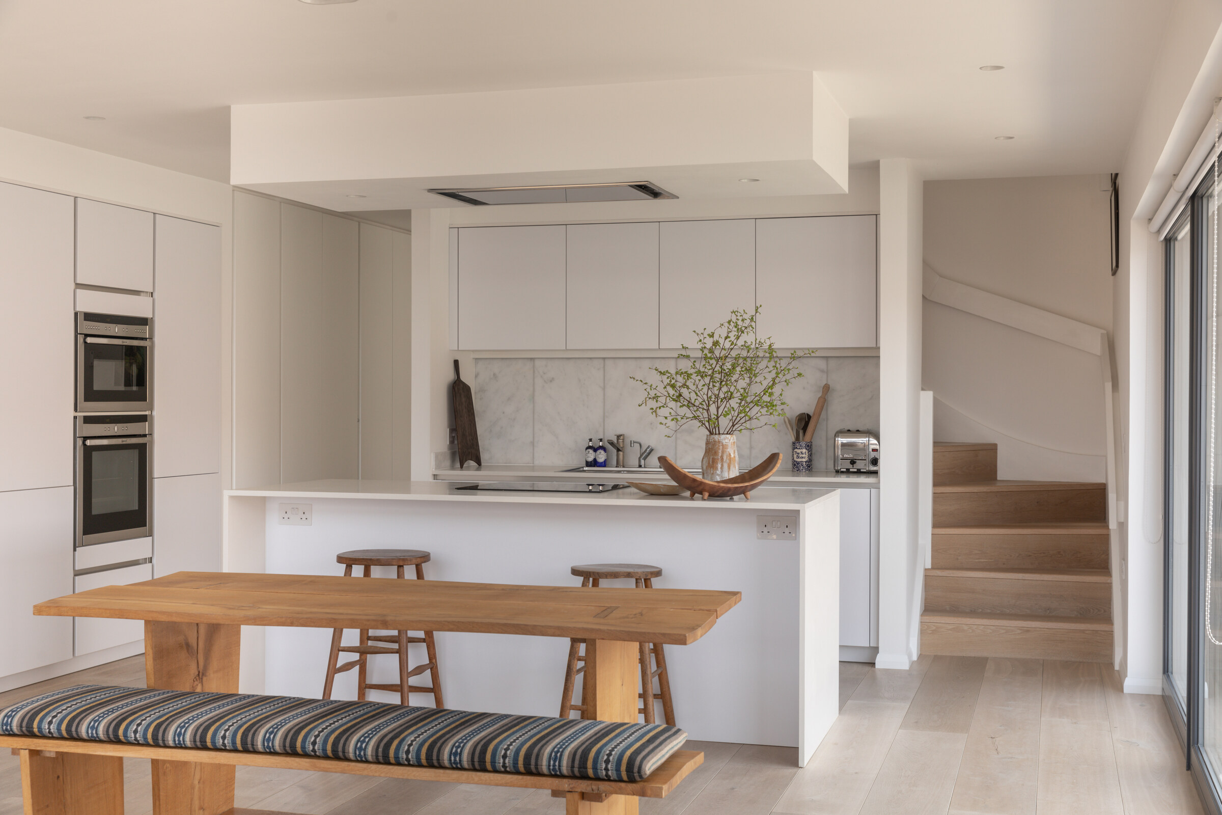 The Net Store’s white kitchen, with a long wooden table and striped bench, and the stairs rising to the mezzanine.