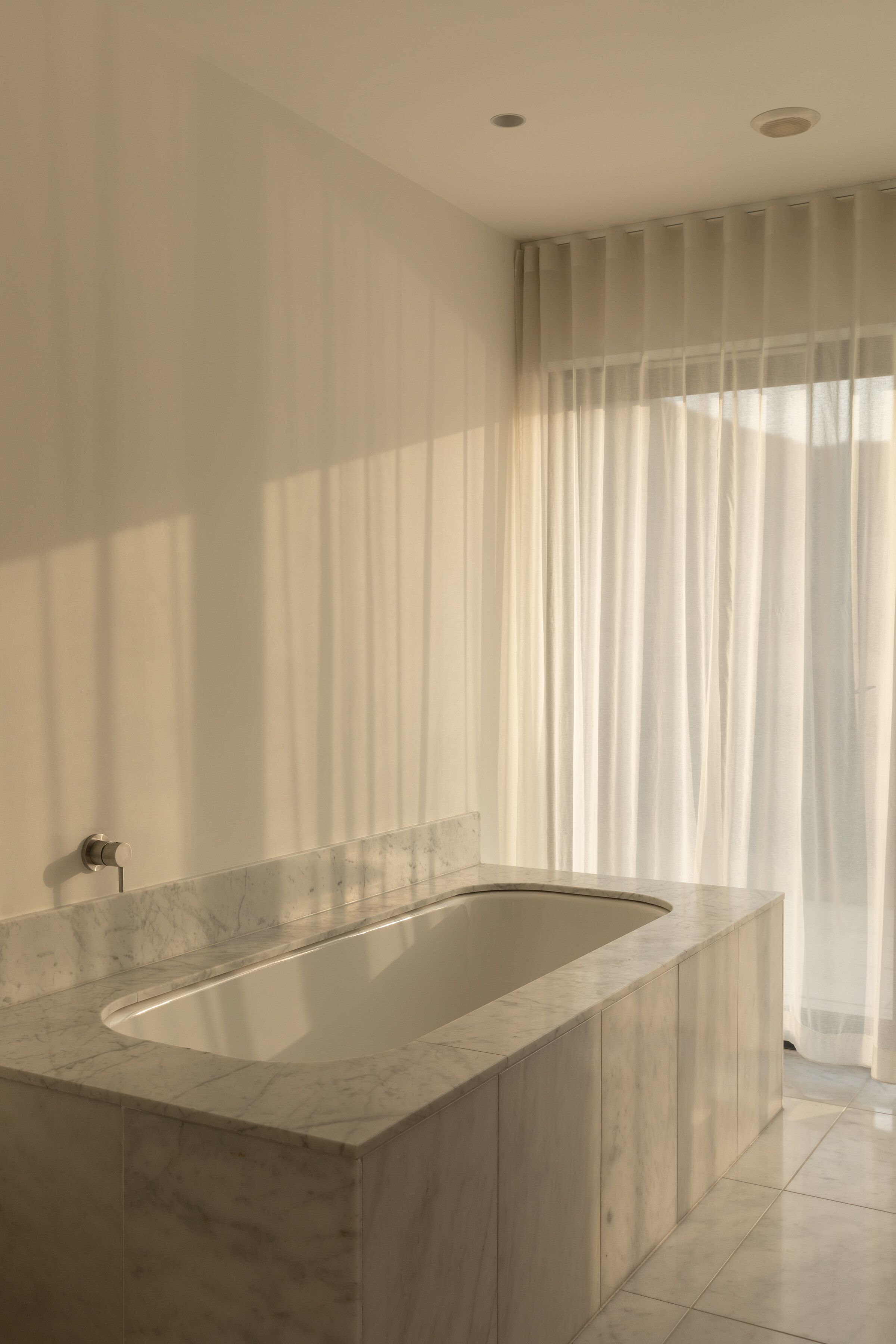 The Net Store’s bath, set in pale marble beneath sheer curtains.