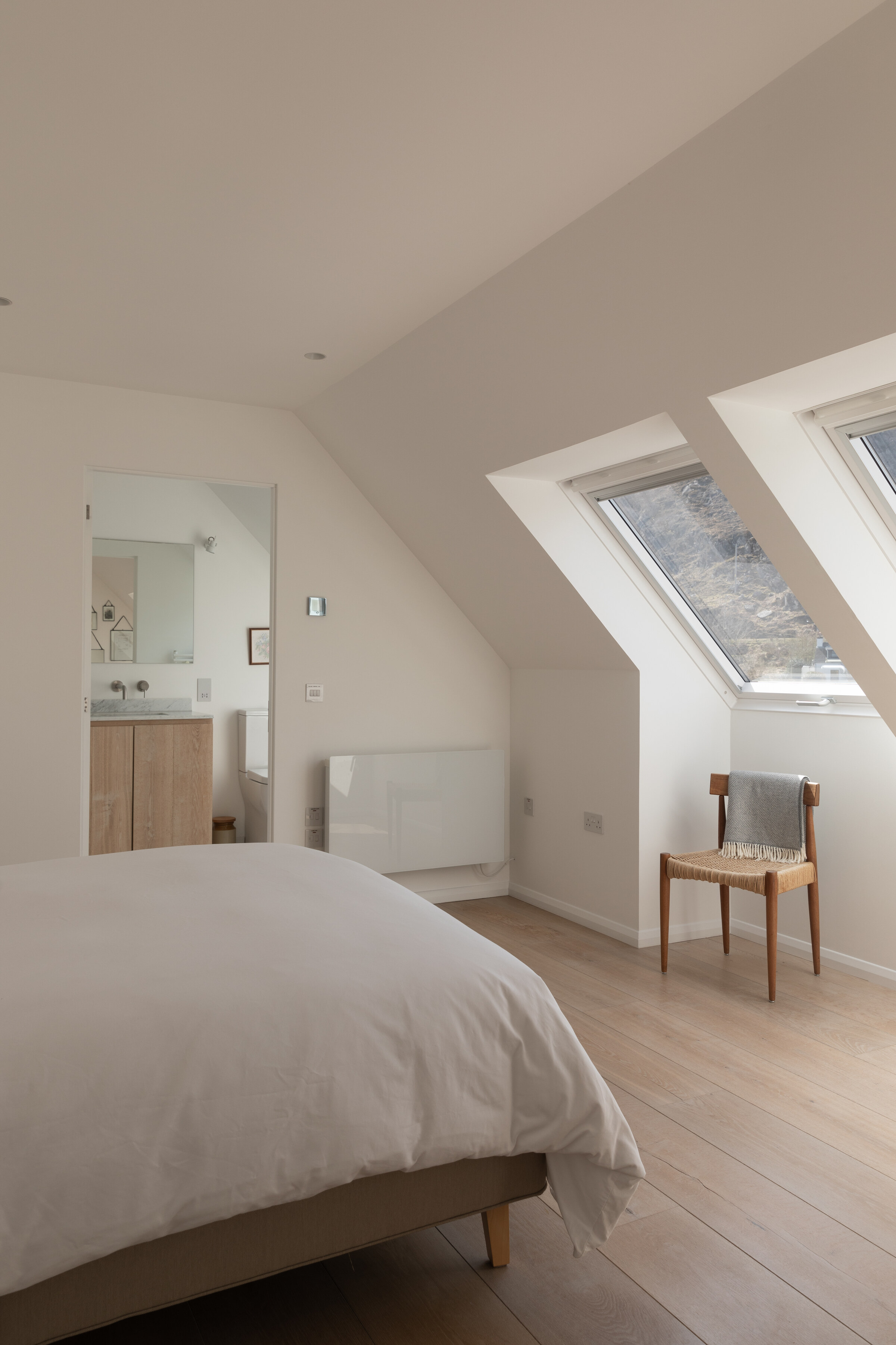 The Net Store’s upstairs bedroom under the slope of the roof, with two skylights and a wooden chair.