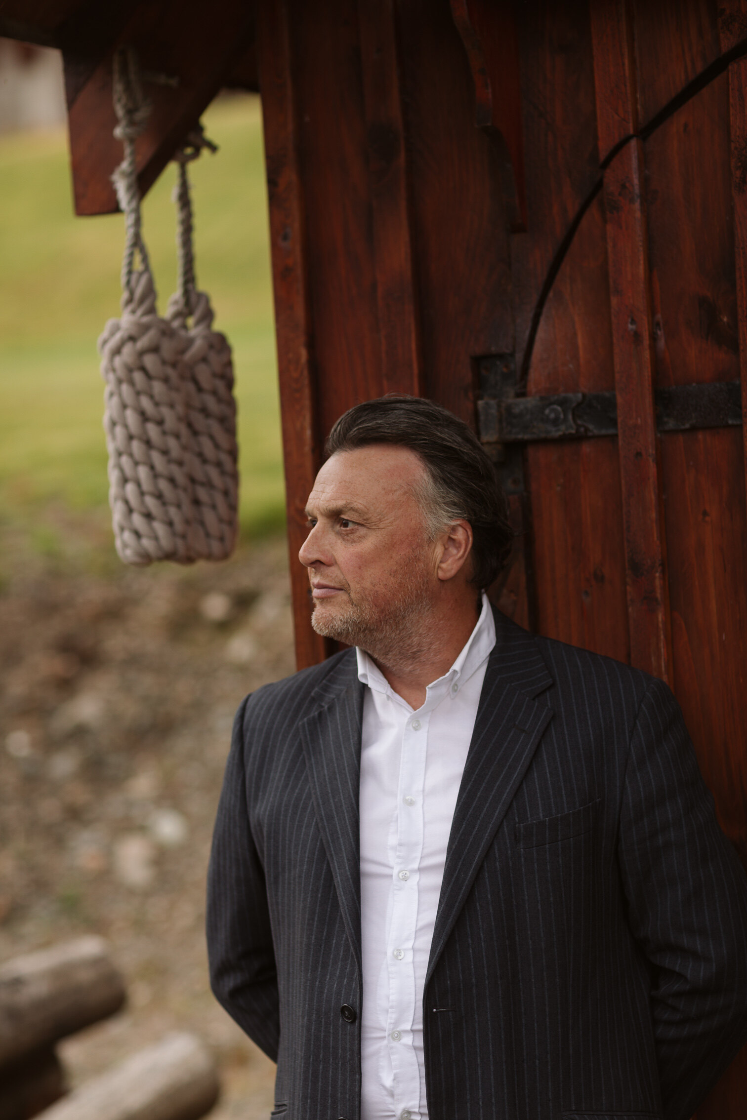 Iain Hopkins in a pinstripe jacket beside the boathouse door at Woodside Lodge, a coiled rope hanging from the eaves.
