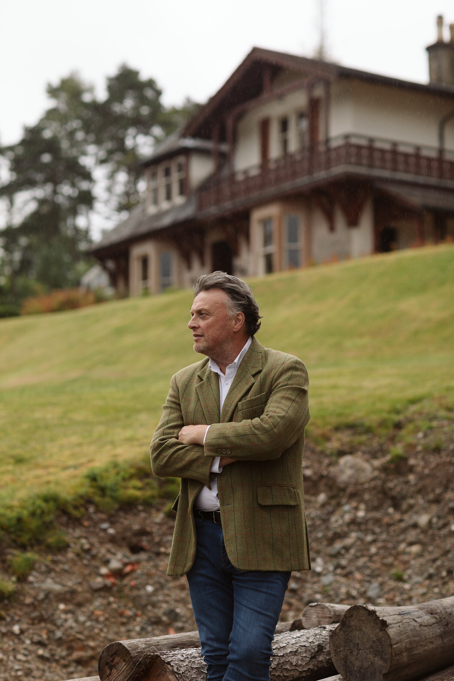 Iain Hopkins stands with his arms folded on the slope below the Victorian lodge at Woodside, its veranda and gables behind him.