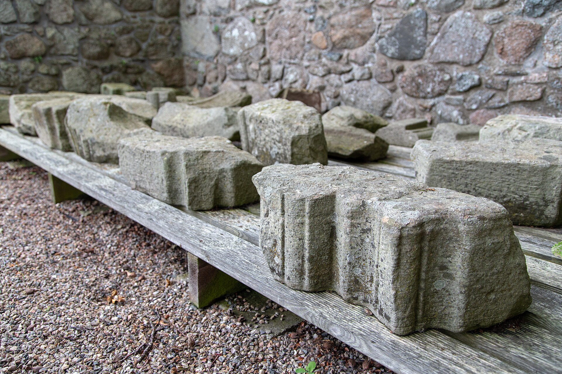 Carved stone panels and fragments laid along a shelf against the rubble wall of Kinkell Church.