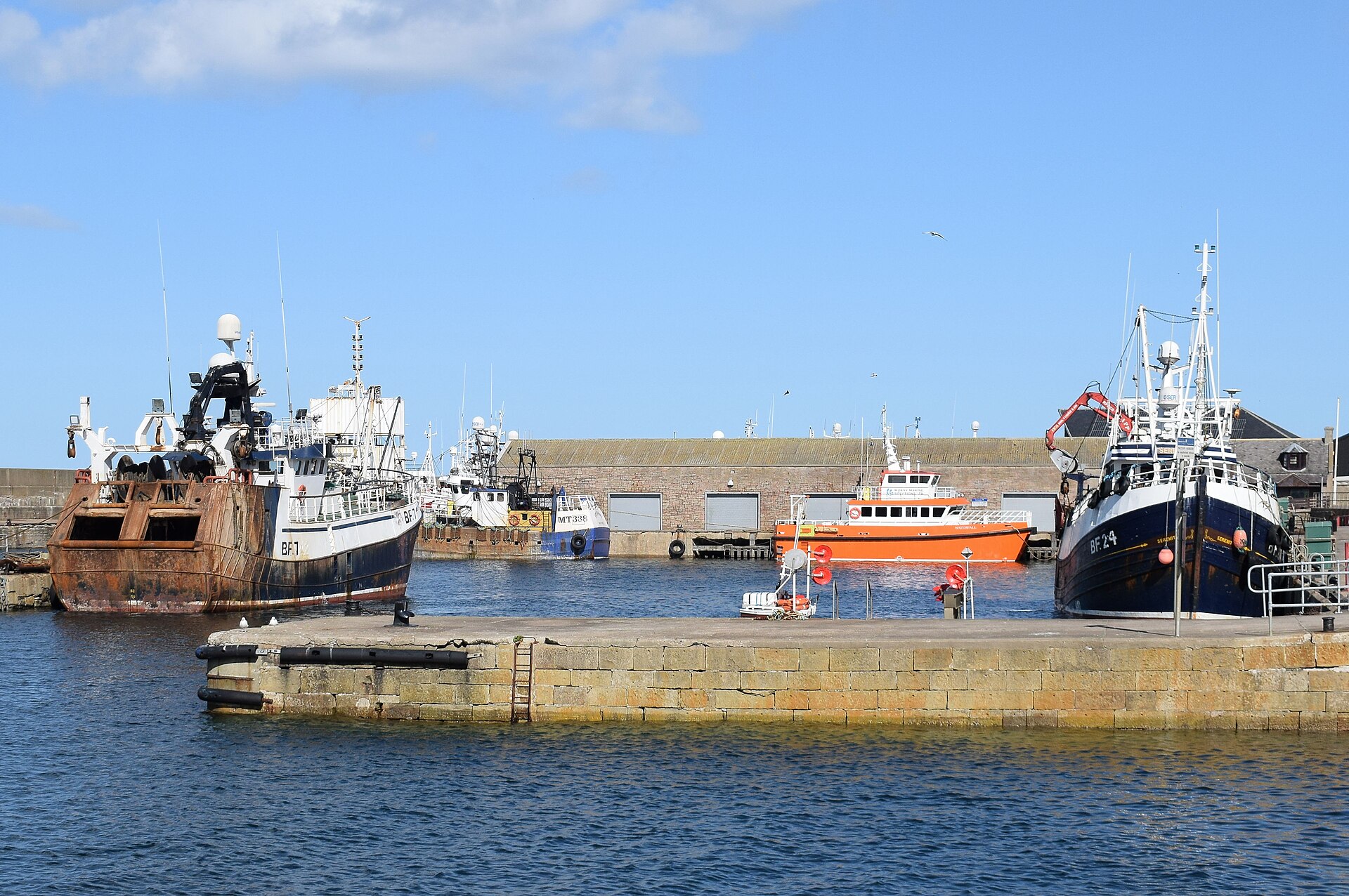 Fishing boats moored in the basin of Macduff harbour under a clear sky.