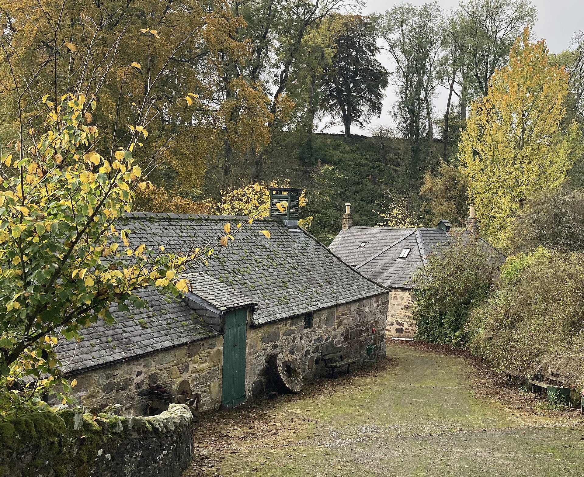 The old stone mill buildings of Benholm among autumn trees.