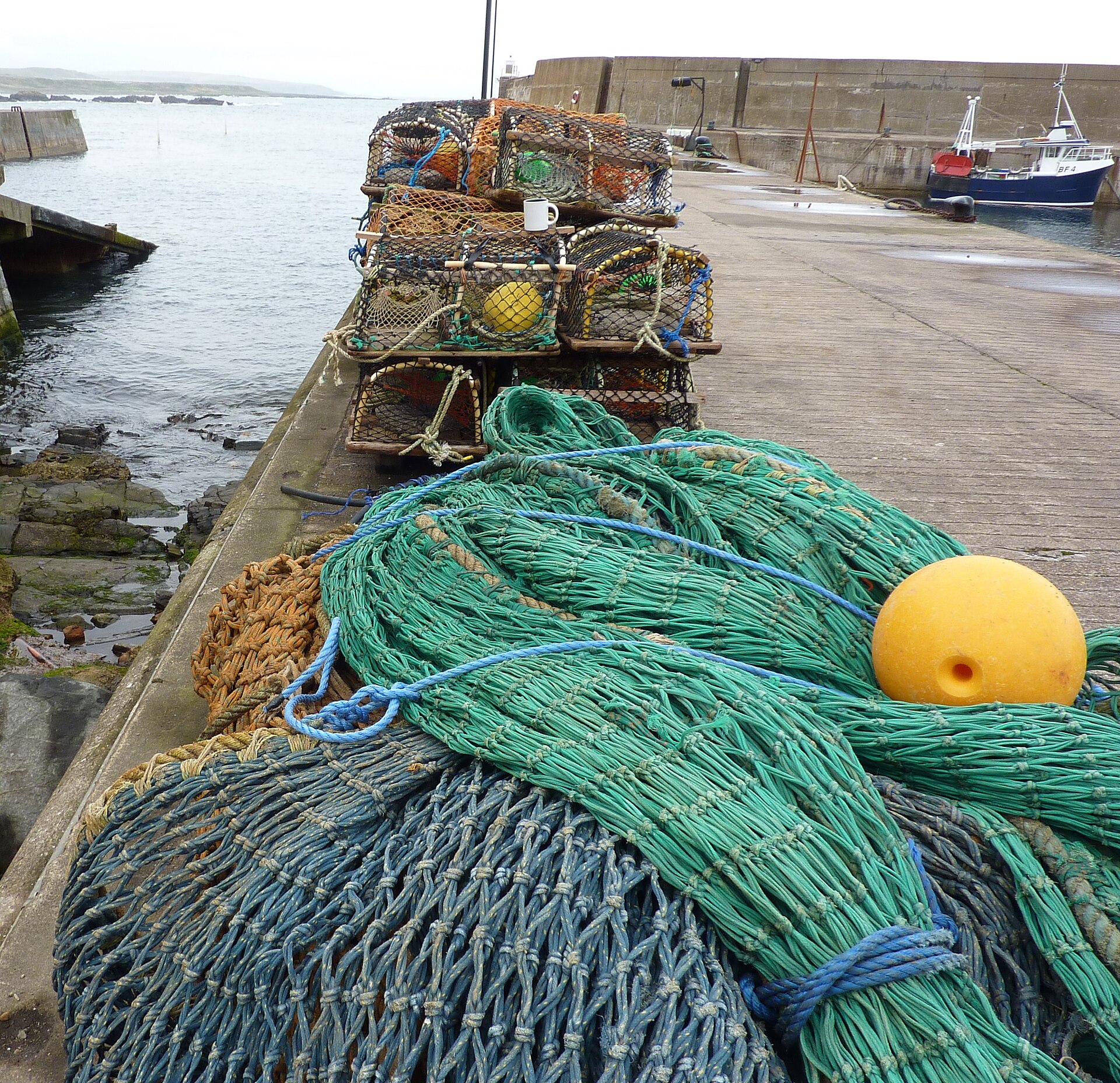 Coils of green net and a yellow float by the lobster creels on Whitehills harbour.